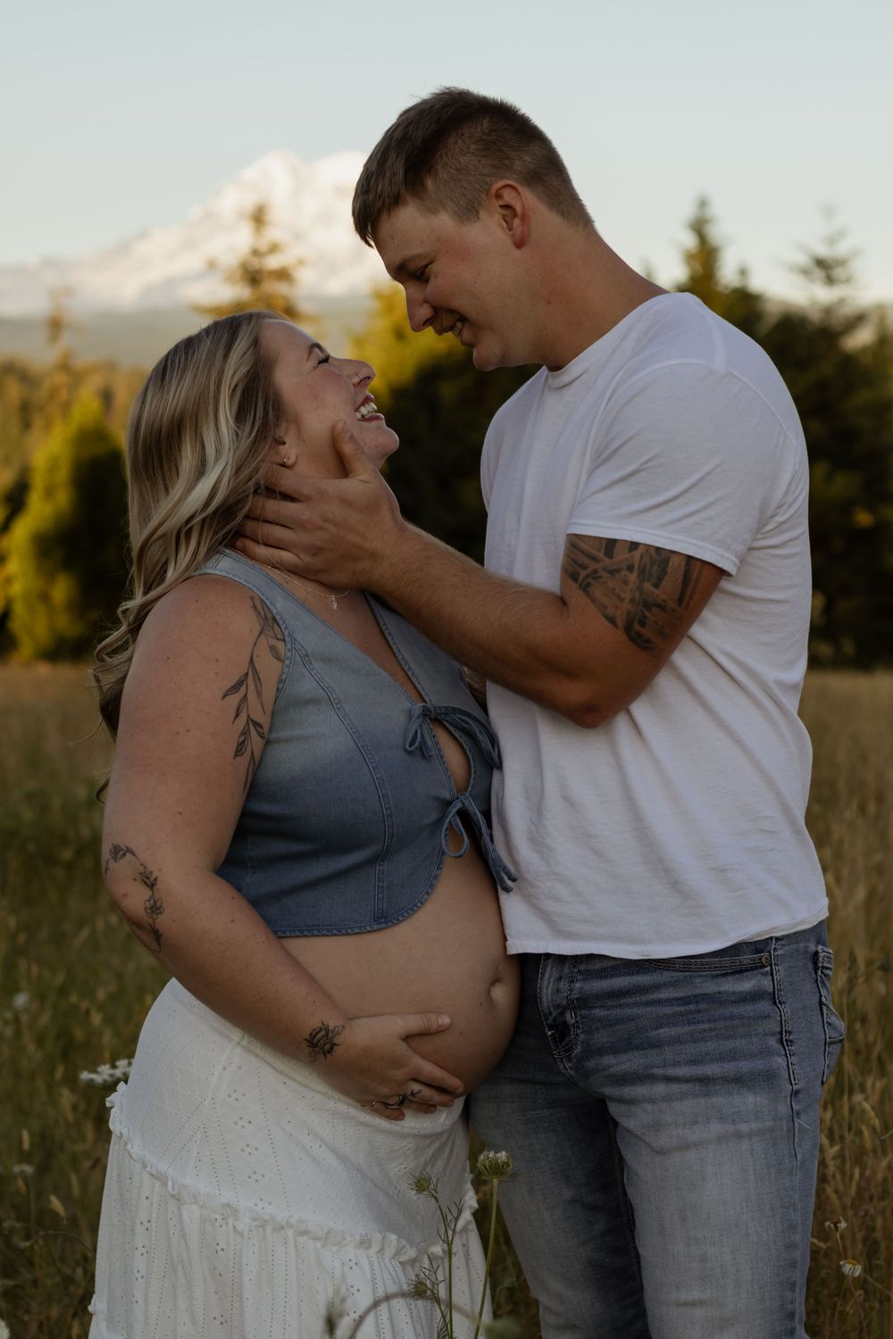 Pregnant couple embracing in a field with Mount Rainier in the background during golden hour maternity photoshoot.