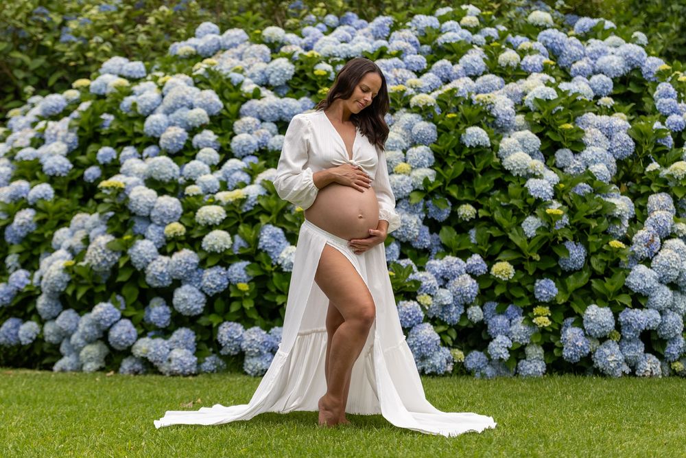 A woman in a white dress poses gracefully in a garden filled with blooming blue hydrangea flowers.