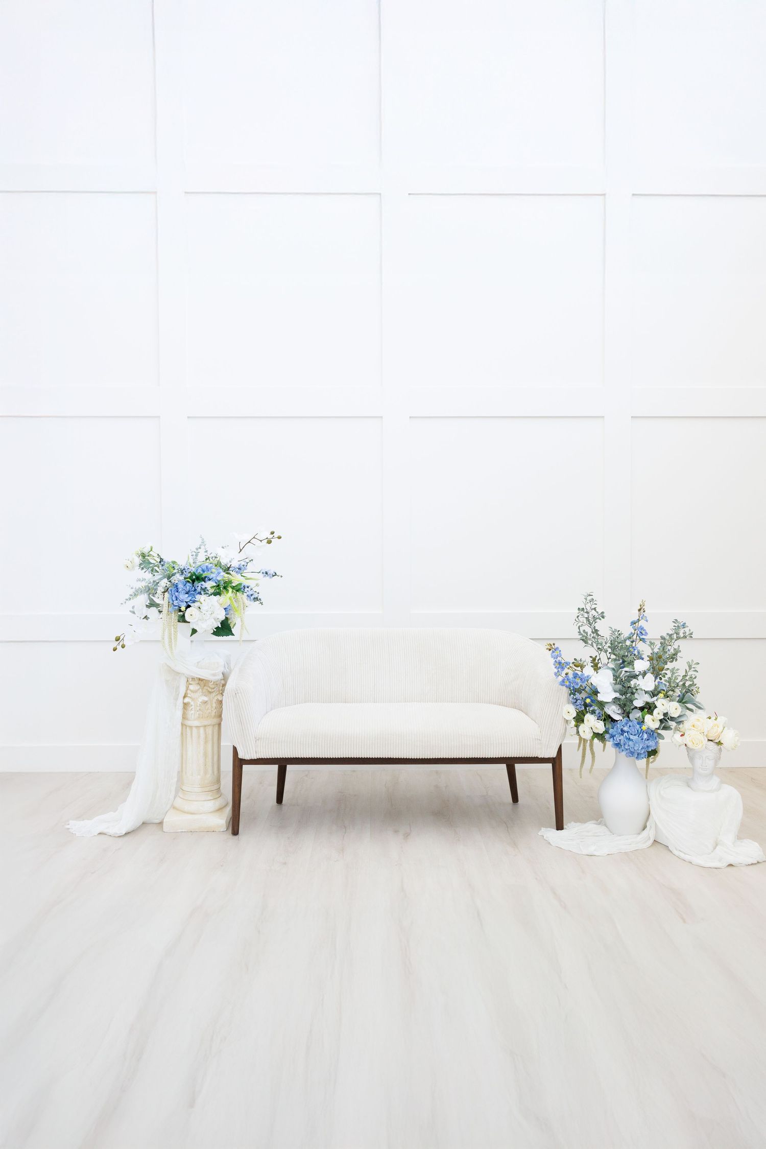 Minimalist white room with blue delphinium flowers and white vases arranged on light wood flooring.