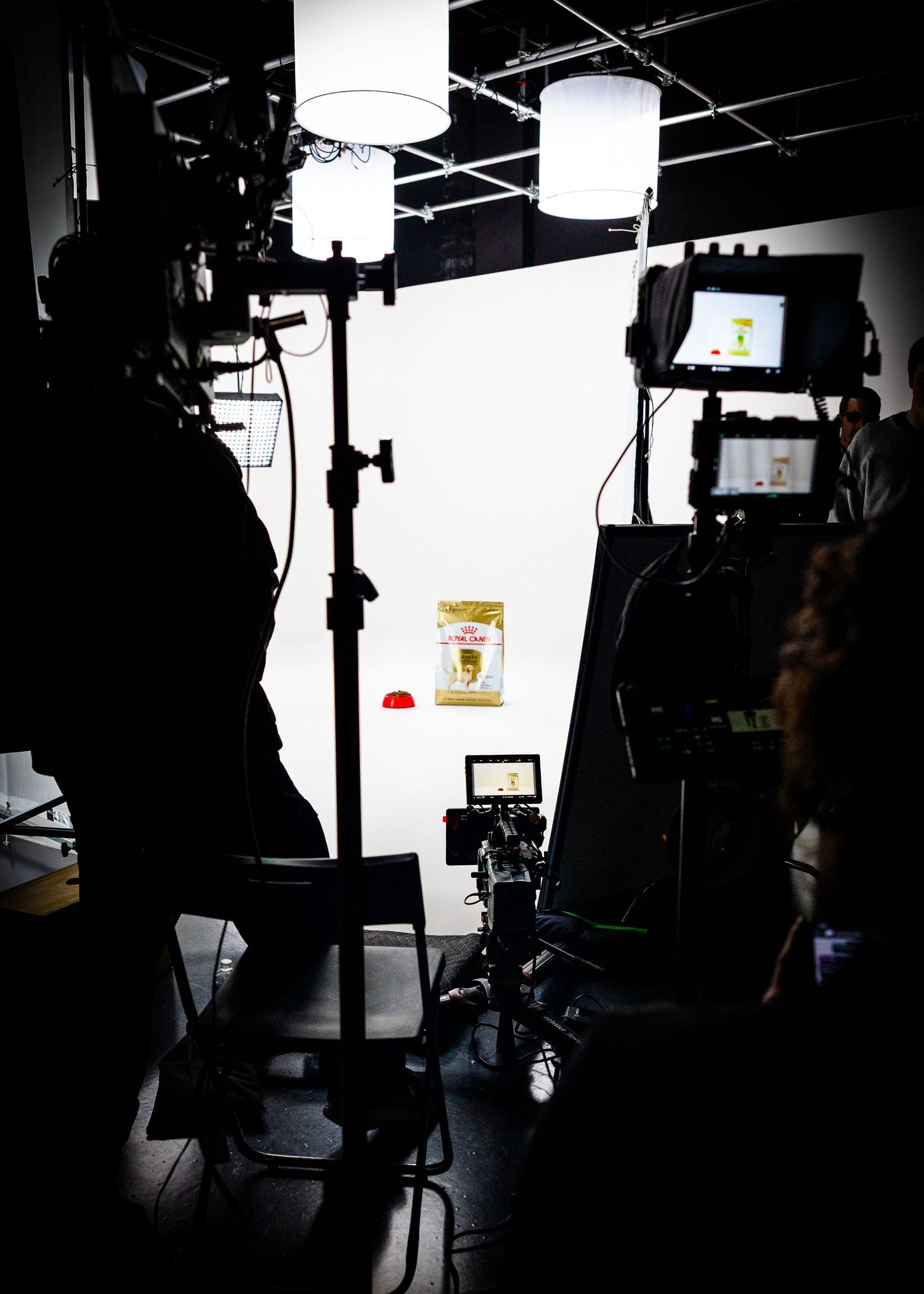Dark silhouettes of film production equipment and lighting gear against a white studio backdrop create a dramatic setup.