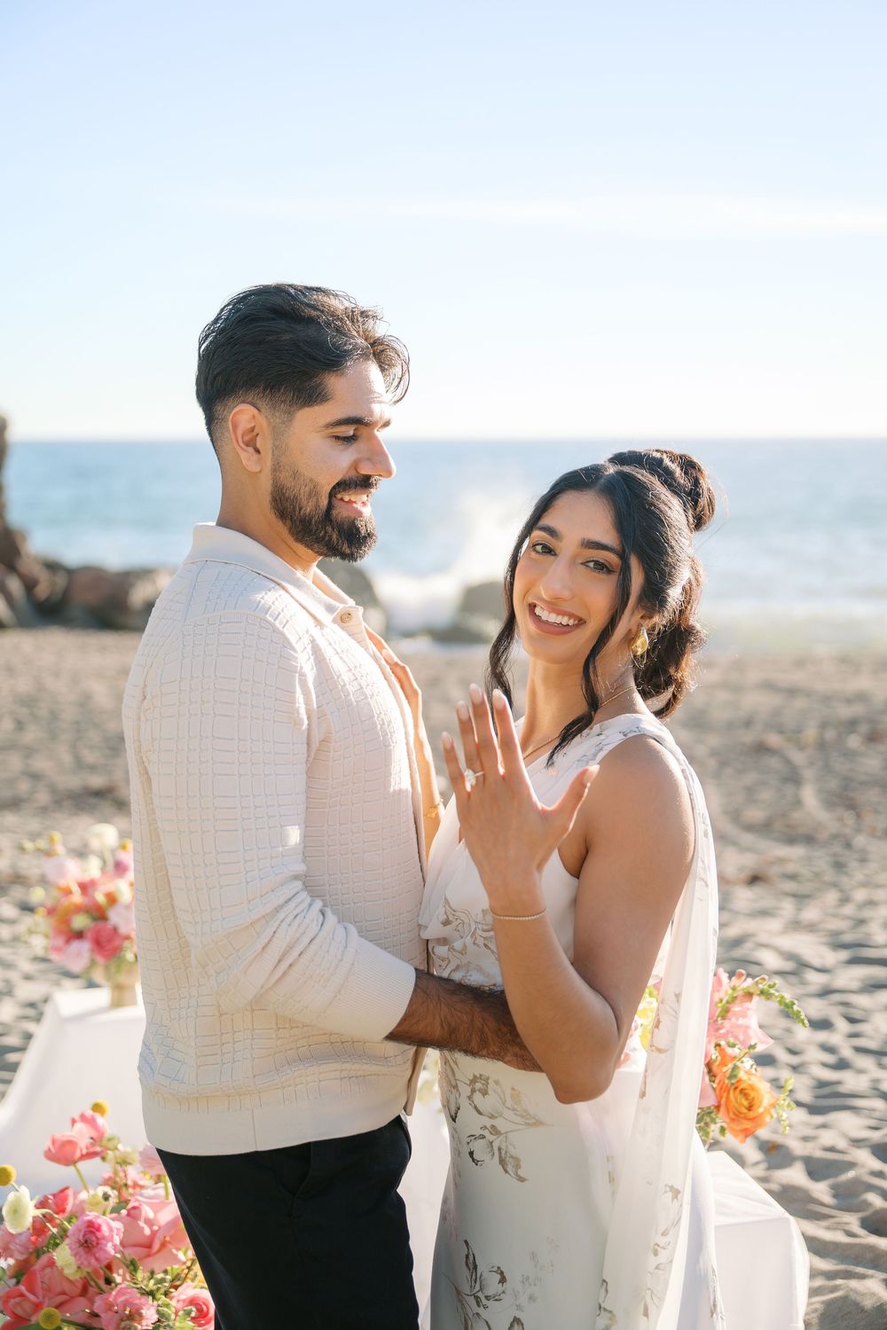 A joyful couple shares emotional moments during their beach wedding ceremony with pink and orange floral decorations.