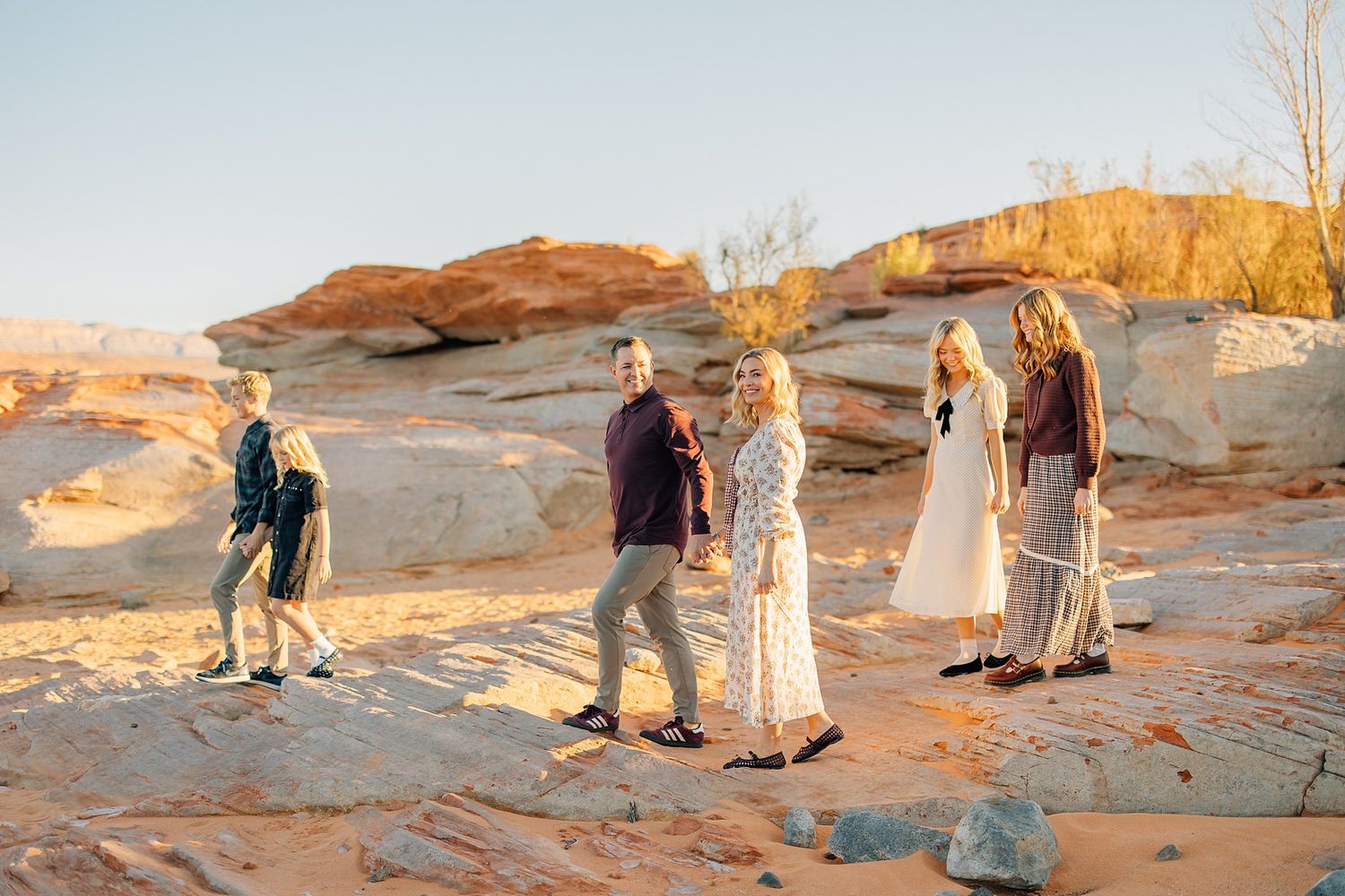 People walking along red rock formations at sunset in a desert landscape.
