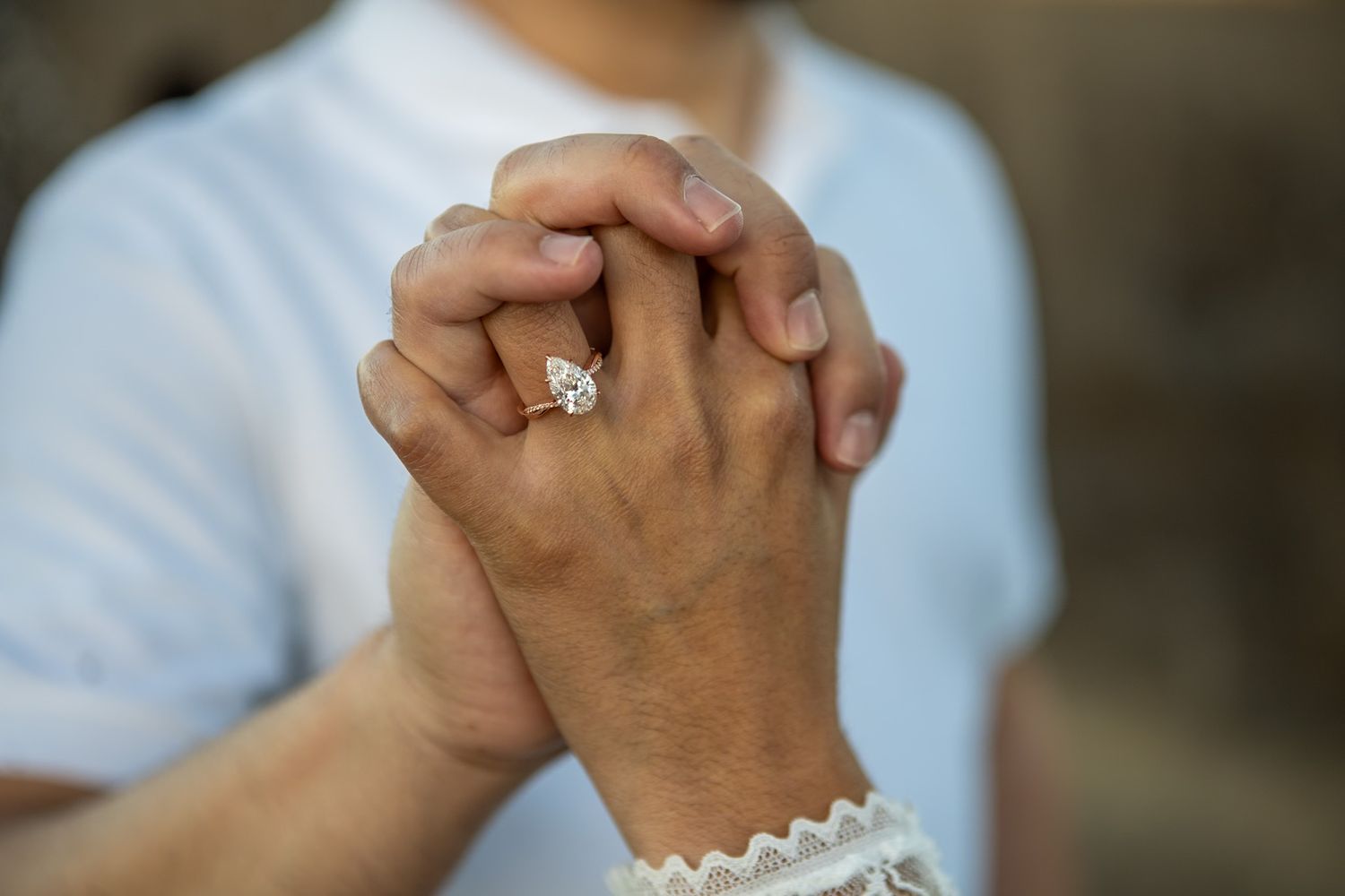 Close-up of clasped hands with an engagement ring, one wearing white lace sleeve detail.