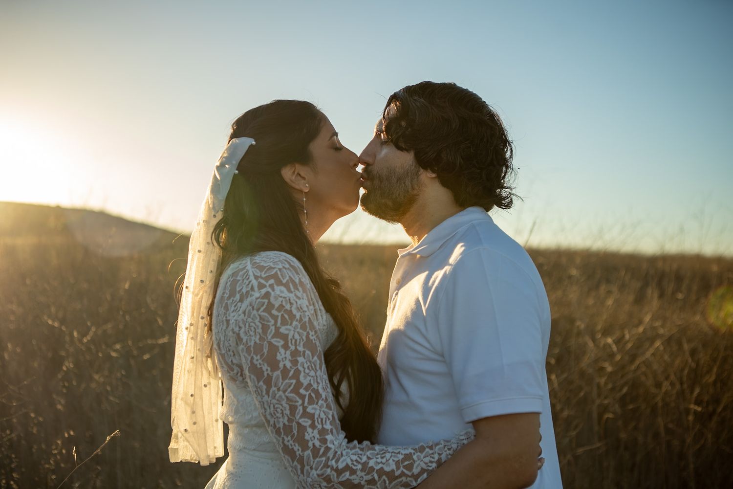 A couple in wedding attire shares an intimate moment at sunset in a golden field.