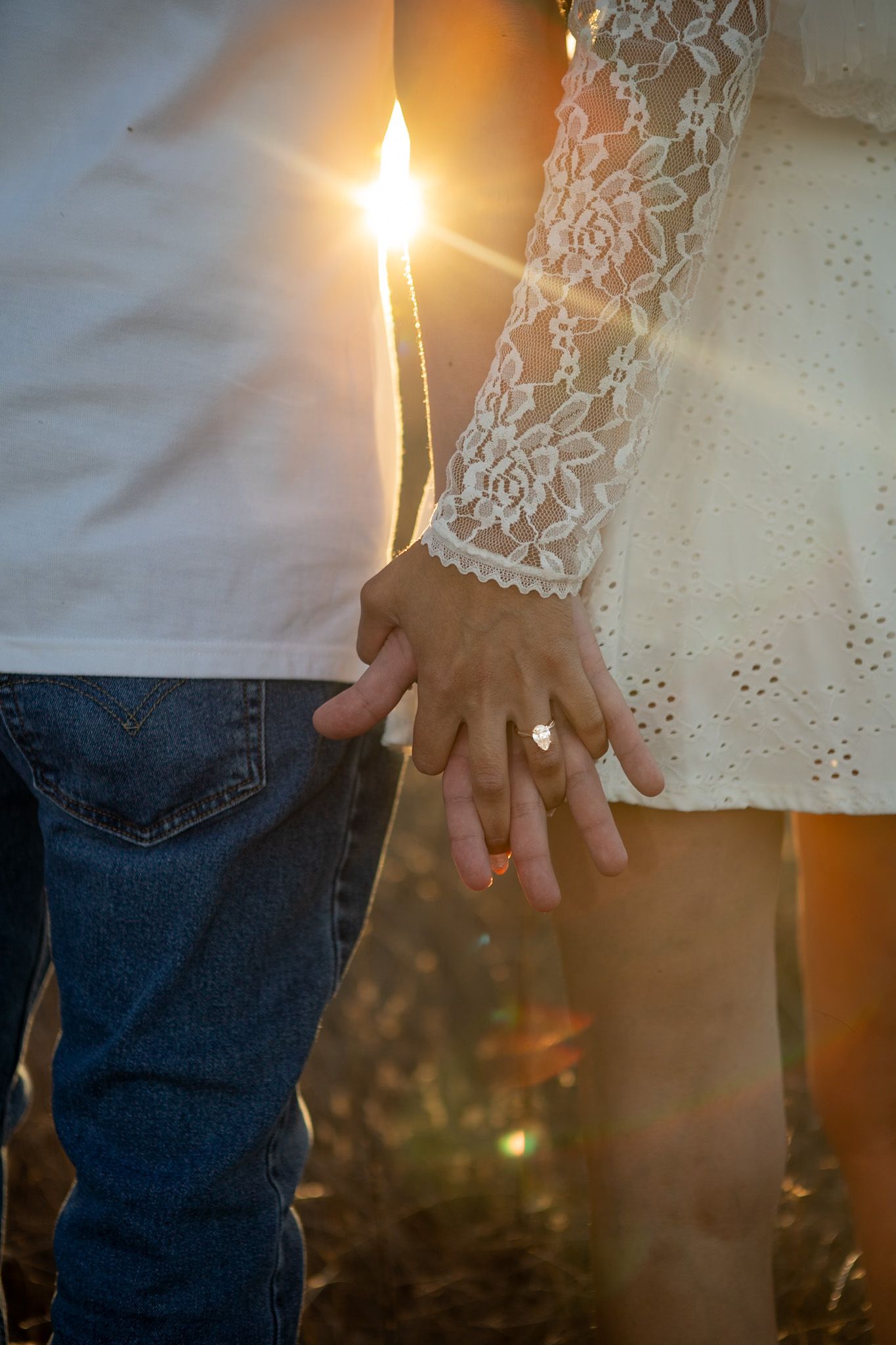 Close-up shot of intertwined hands with sunlight flare creating a romantic silhouette against a blurred outdoor background.