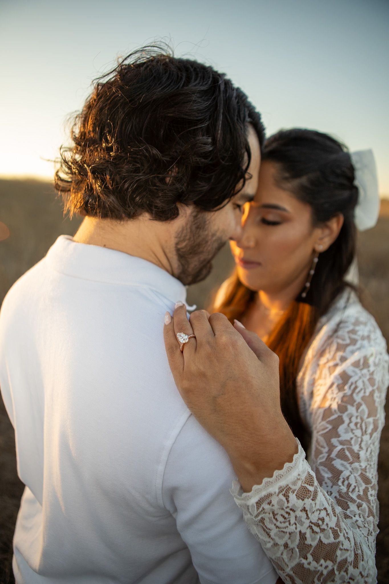 Intimate wedding couple moment captured in silhouette against soft sky, with bride in delicate lace dress.