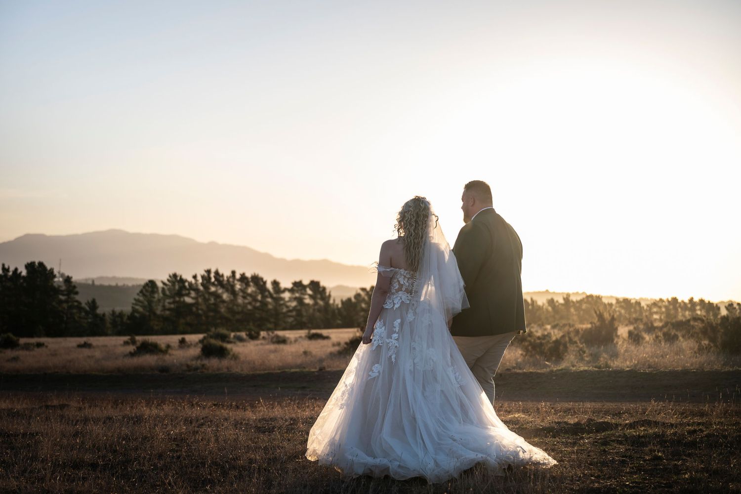 Bride and groom stand together at sunset overlooking a scenic mountain landscape on their wedding day.