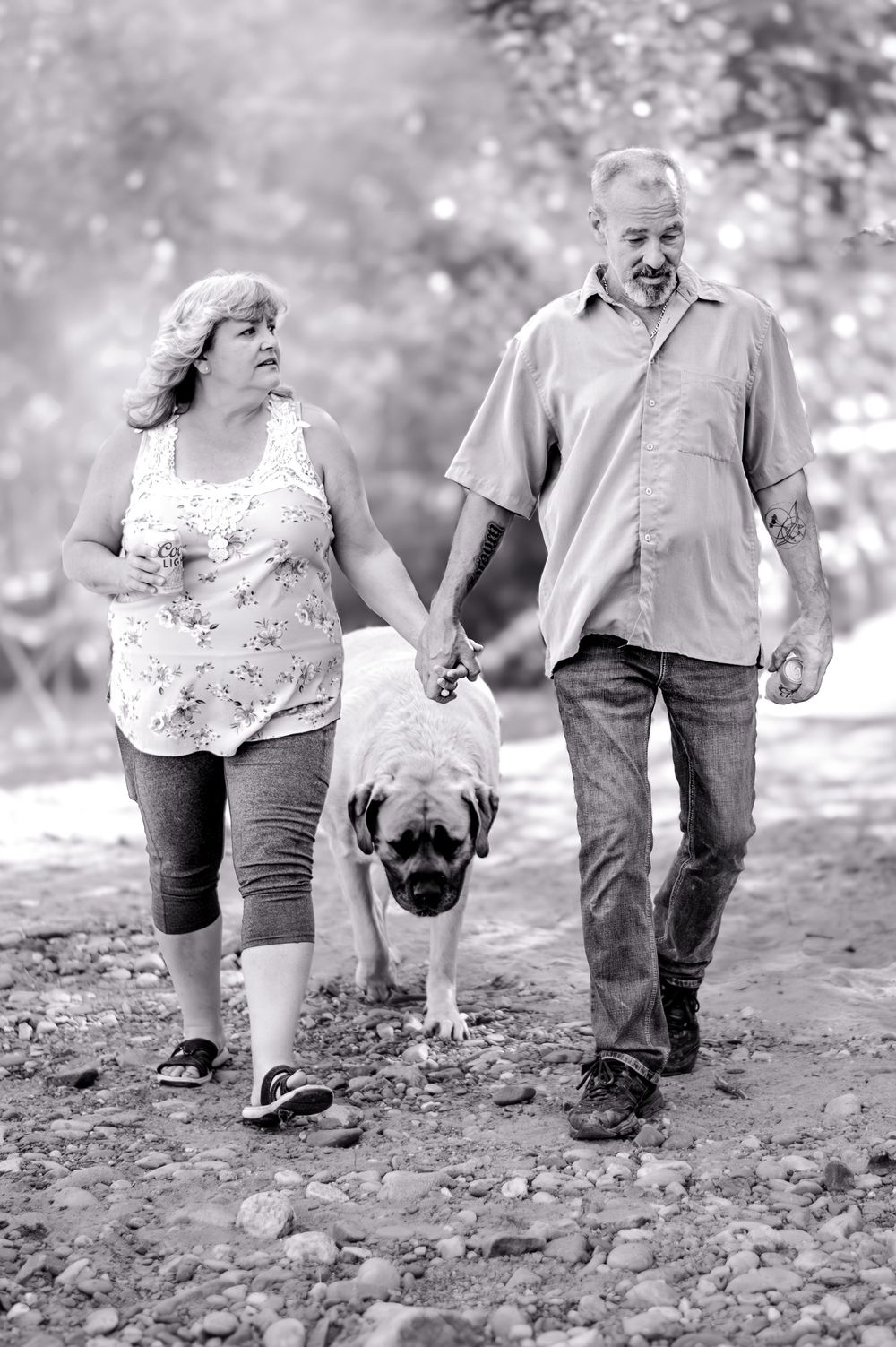 A couple and their pug dog walking together on a rocky path in black and white photography.