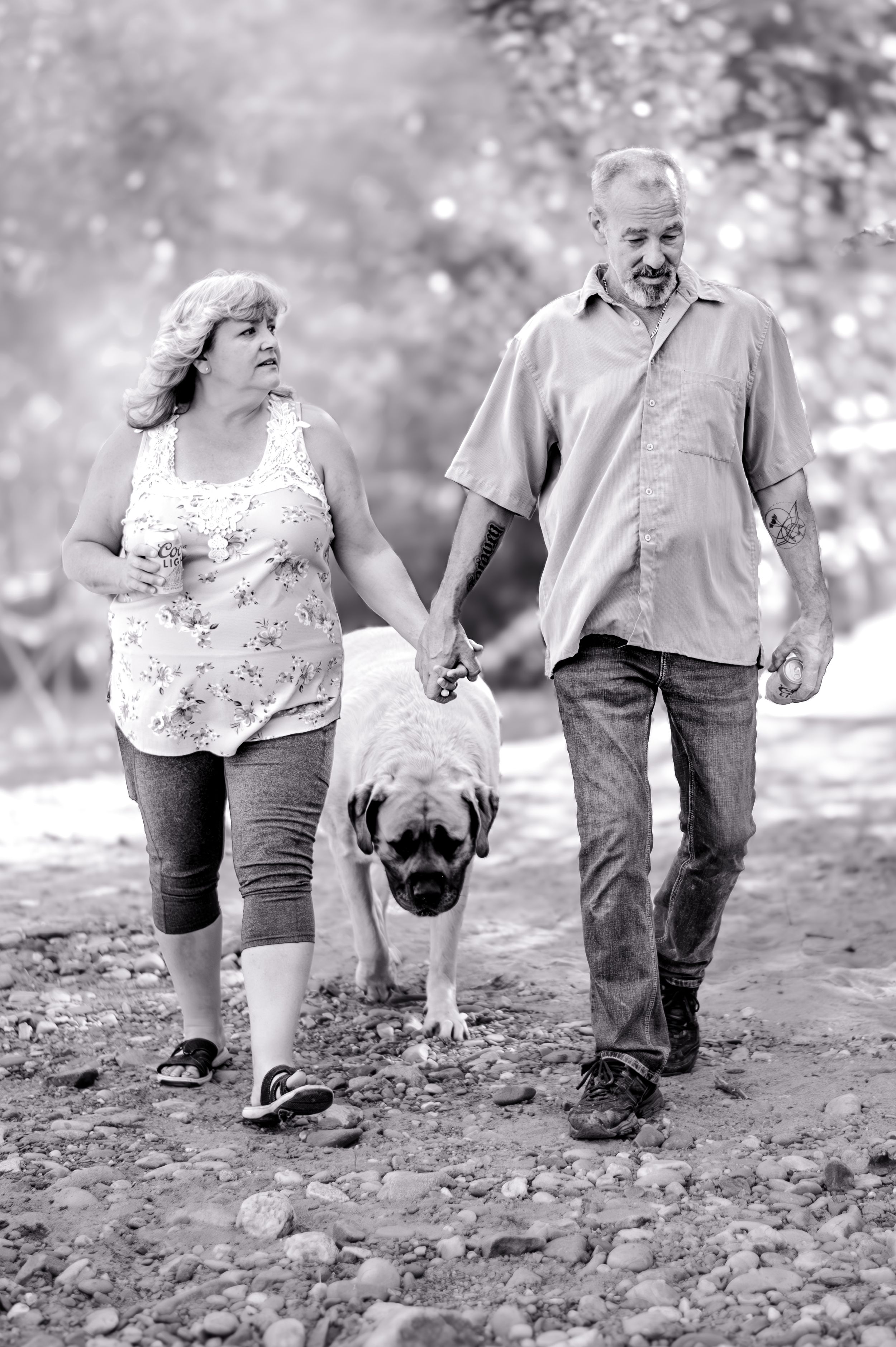 A couple and their pug dog walking together on a rocky path in black and white photography.