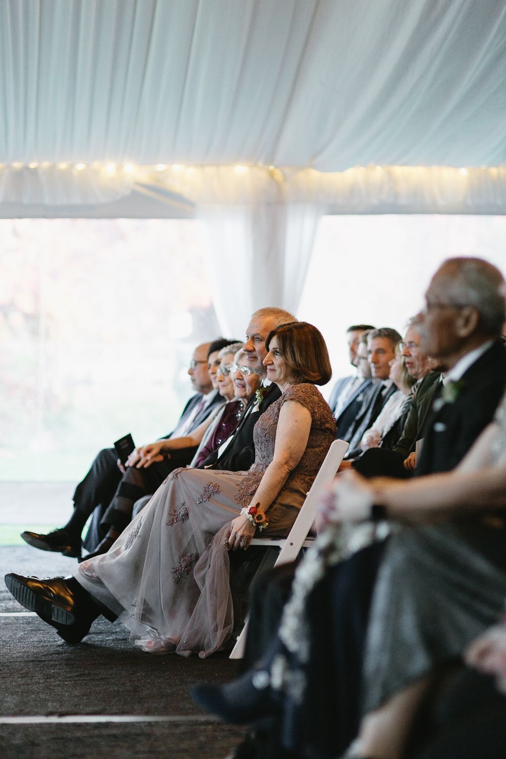 Wedding guests relax with their feet up against a white tent backdrop at an outdoor reception.