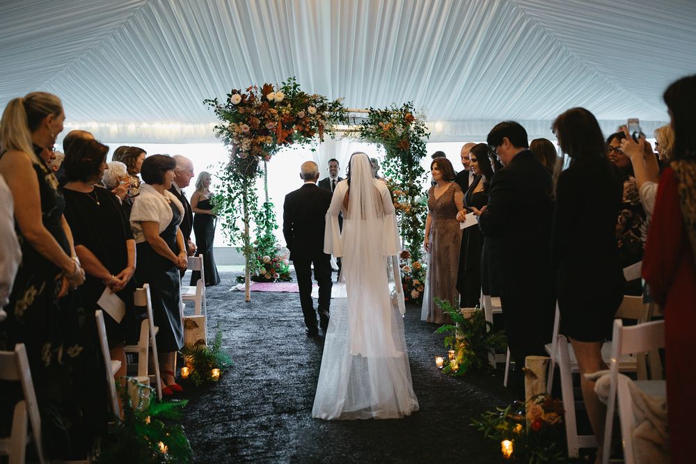 Wedding guests gather under a white tent canopy during an elegant evening celebration.
