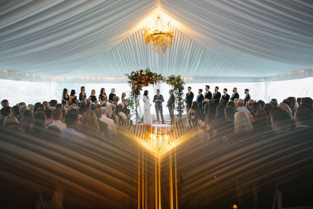 Silhouettes of people stand in line against a bright light shining through a draped fabric ceiling at dusk.