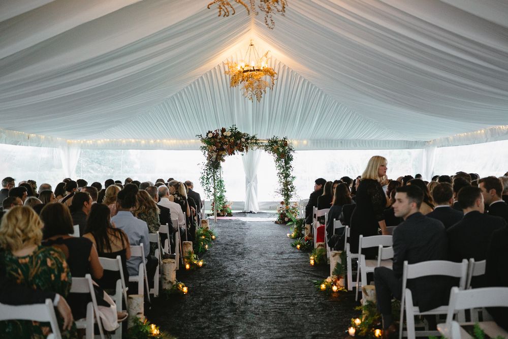 Panoramic view of an elegant wedding ceremony setup under a white tent with rows of chairs and floral decorations.