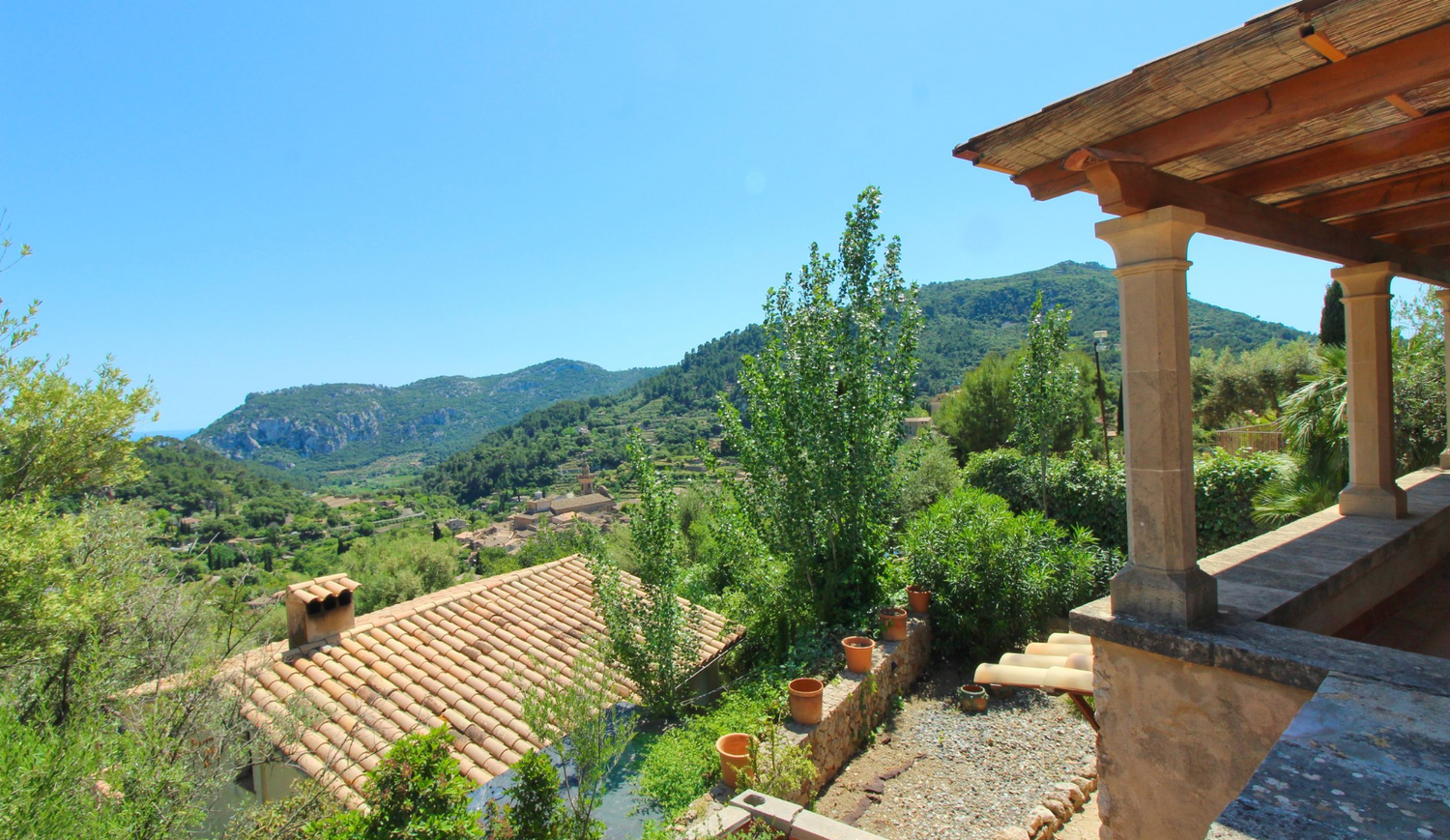 A scenic mountain landscape with rustic adobe buildings and terracotta roofs nestled against green hills and blue skies.