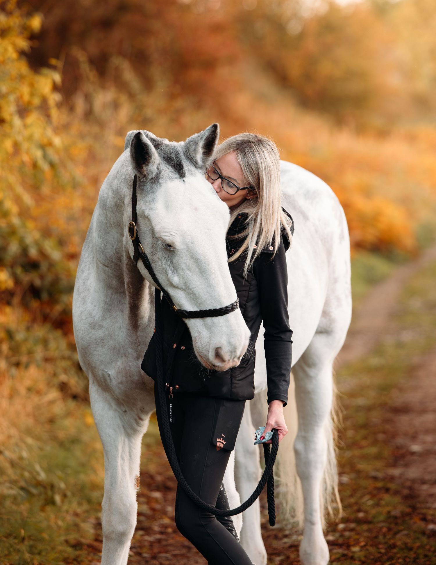 White horse stands next to person in black outfit during autumn sunset.