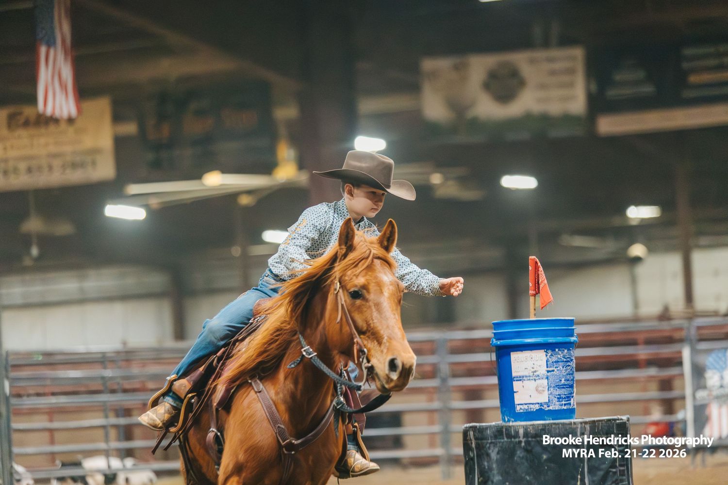 Barrel racing competition at a rodeo arena with horses and riders navigating around orange safety cones.