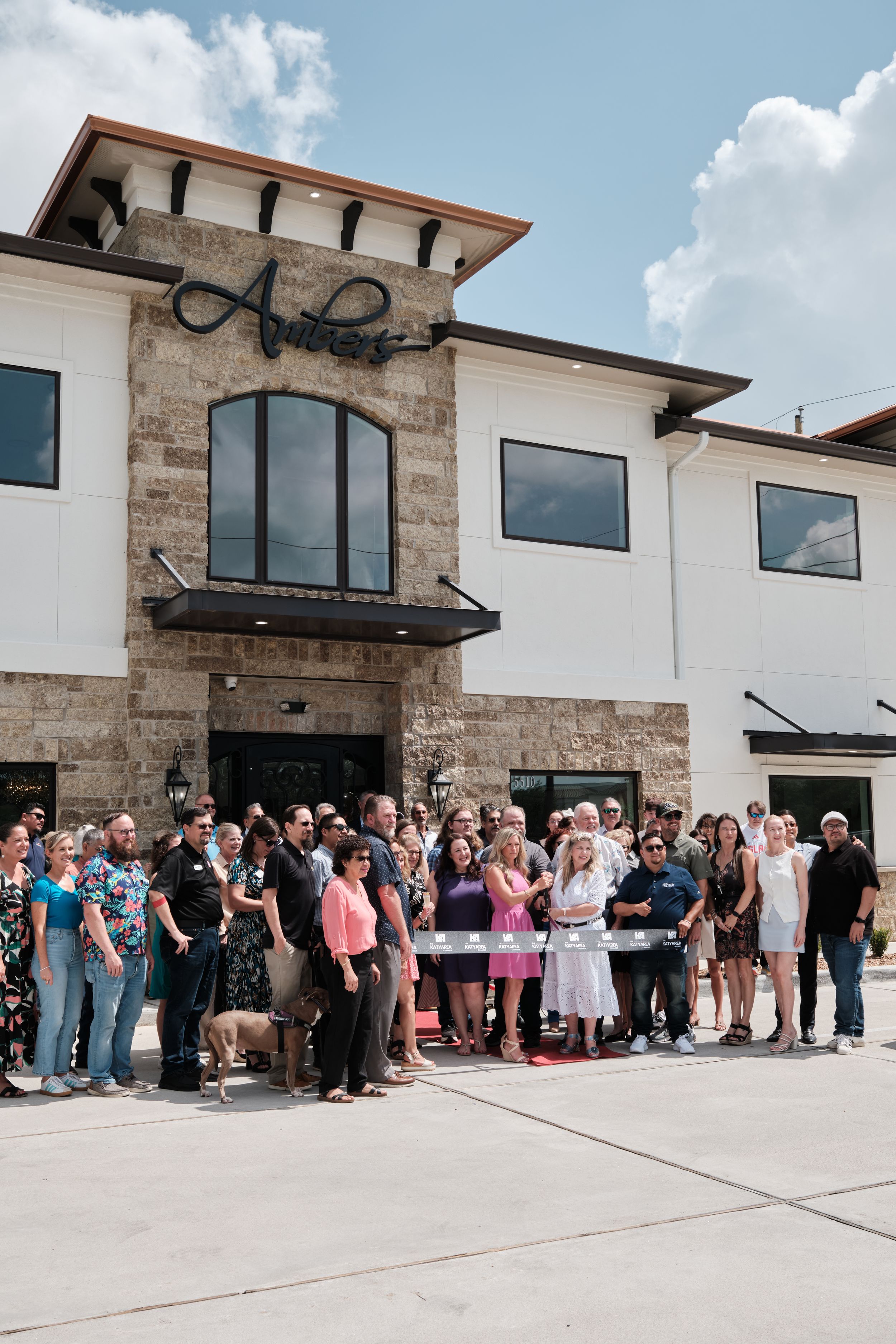 A crowd gathers for a ribbon-cutting ceremony outside a stone and white modern commercial building named Antlers.