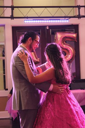 Young couple sharing a slow dance at a quinceañera party with a number 15 balloon decoration in background.