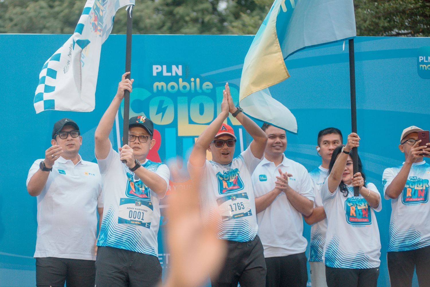 People in white and blue uniforms wave flags and cheer during a PLN mobile event.