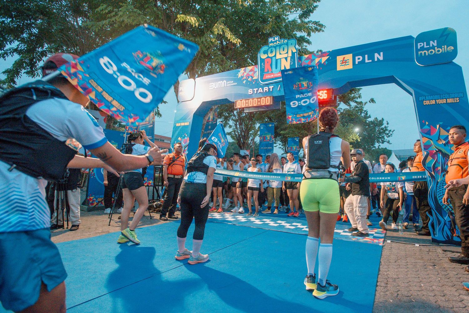 Participants gather at a running event with blue banners and tents set up along the course.