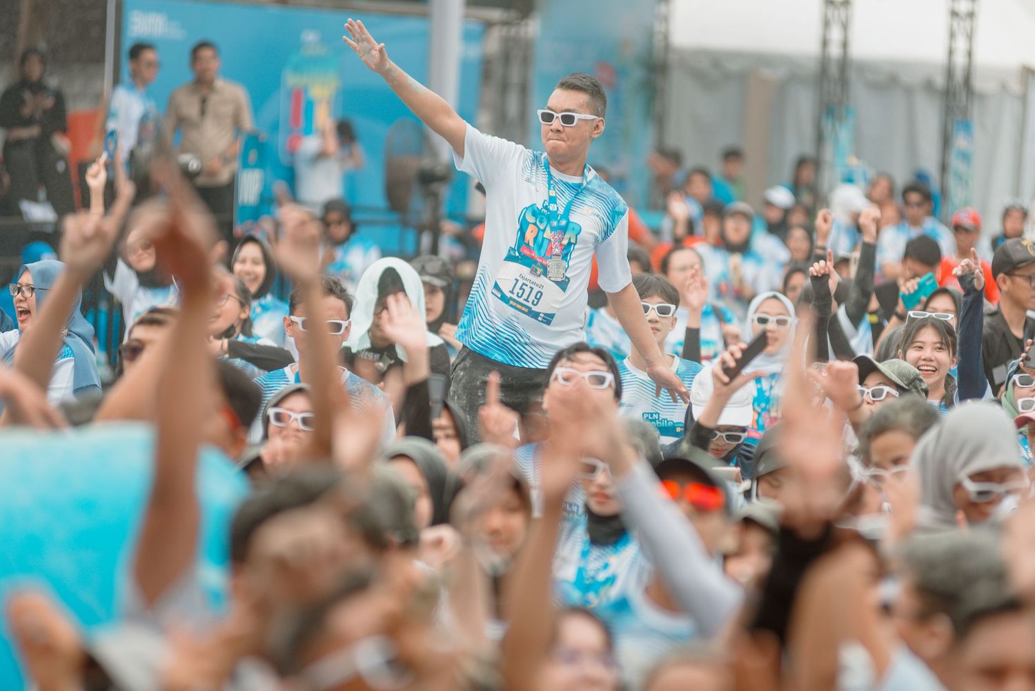 A large crowd of sports fans cheering and waving their arms at an outdoor stadium event.
