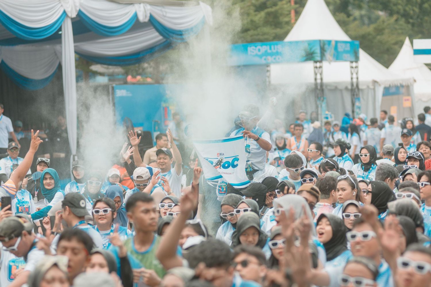 Large crowd of sports fans in light blue team colors celebrate with smoke effects at an outdoor event.