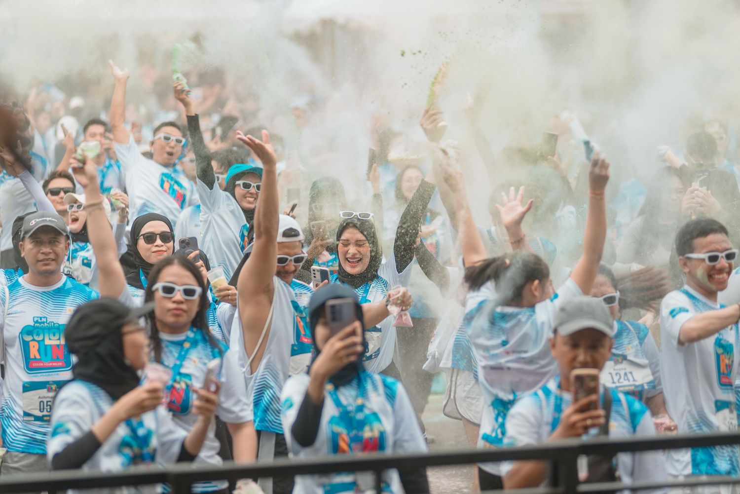 Energetic crowd wearing matching light blue shirts raises their arms in celebration at an outdoor event.