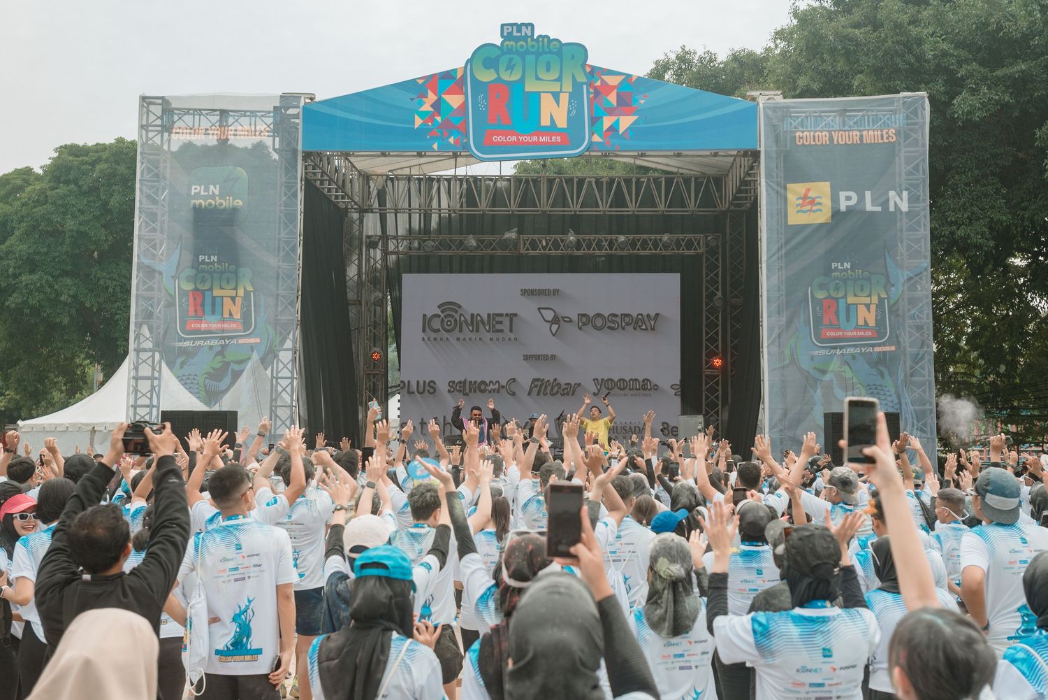 Crowd of people in light blue shirts gather at an outdoor event with banners and promotional displays.