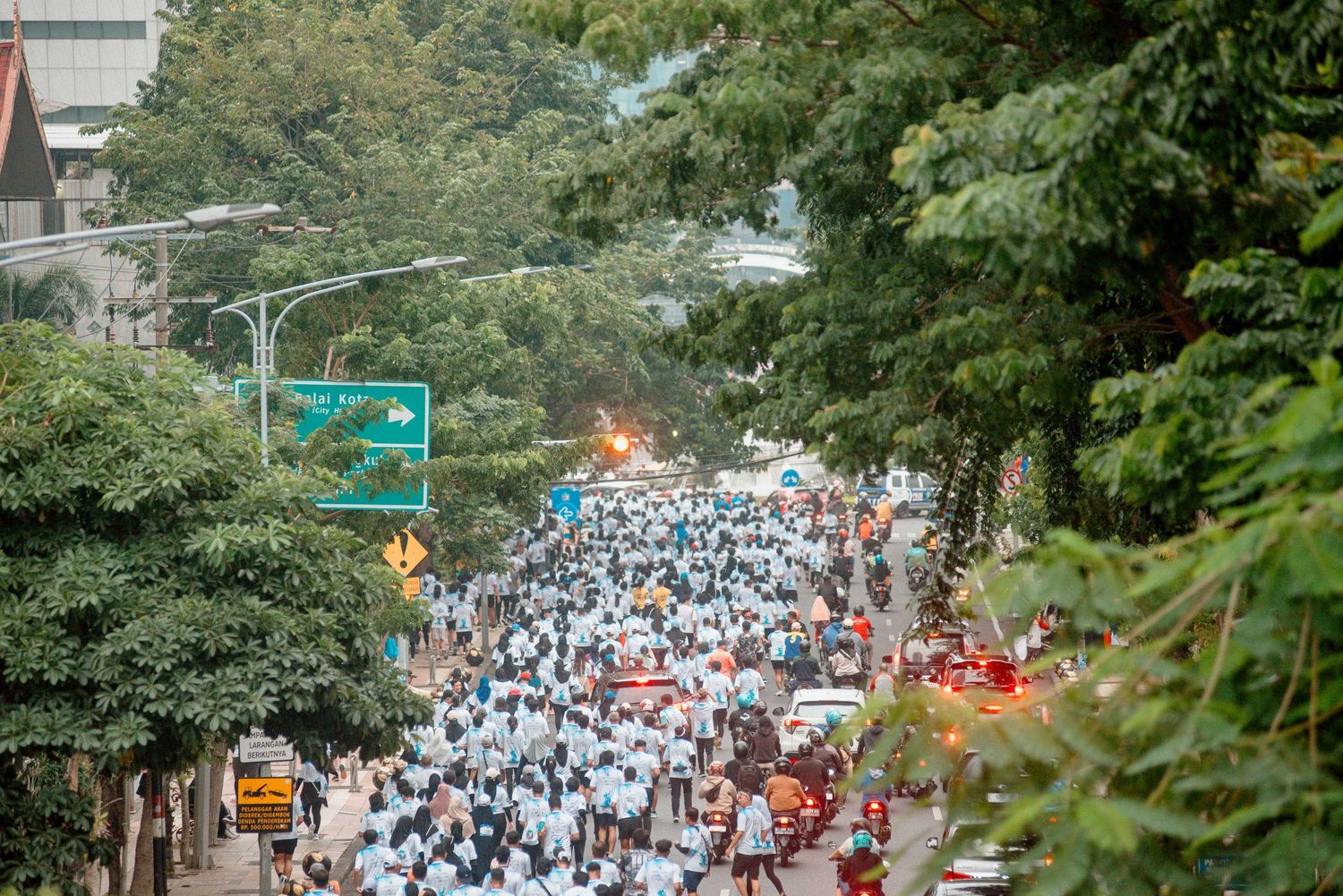 Large crowd of people in white clothing walking down a tree-lined street during a public gathering or protest.
