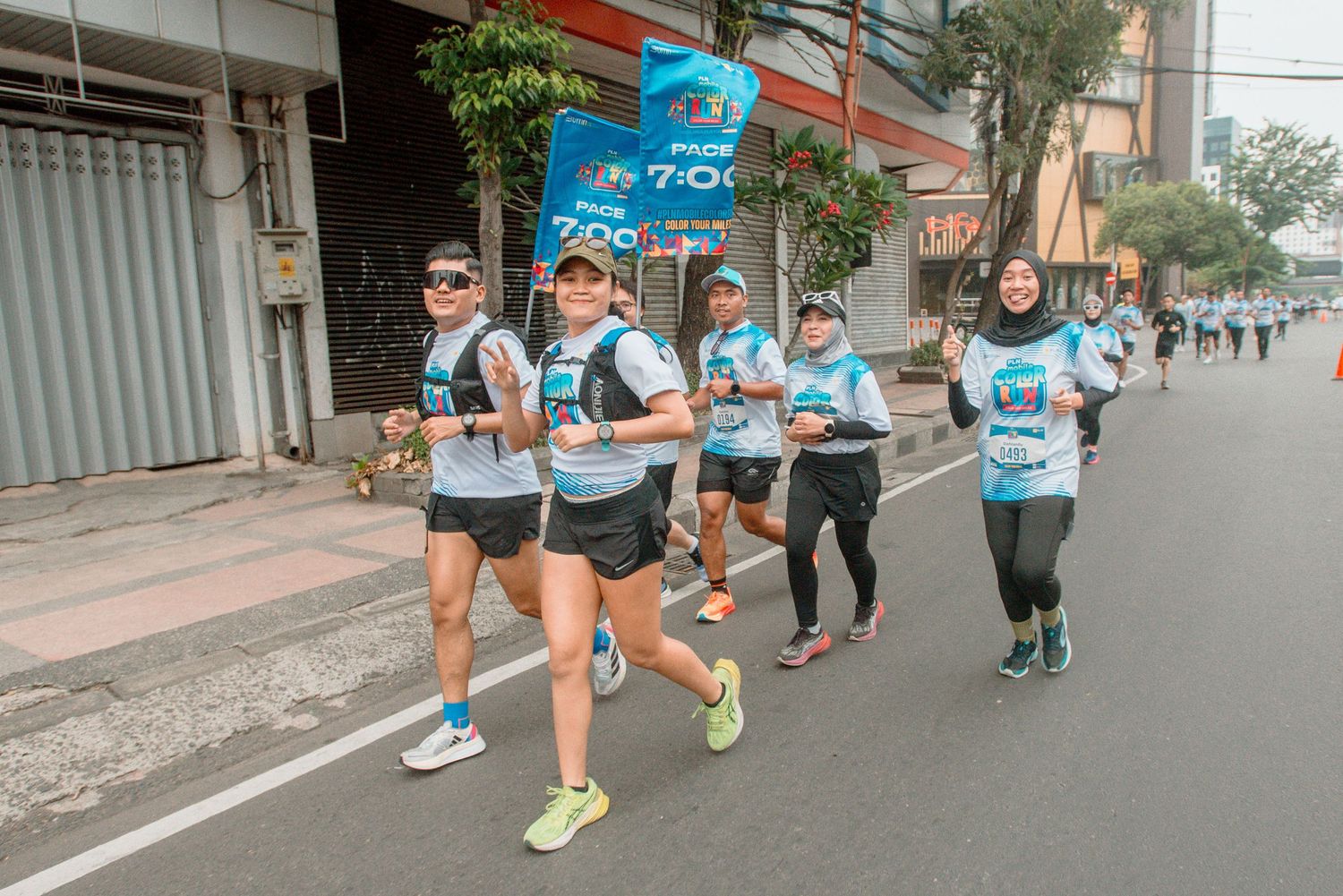 Runners participating in a marathon or road race on a city street with spectators watching along the sidewalk.