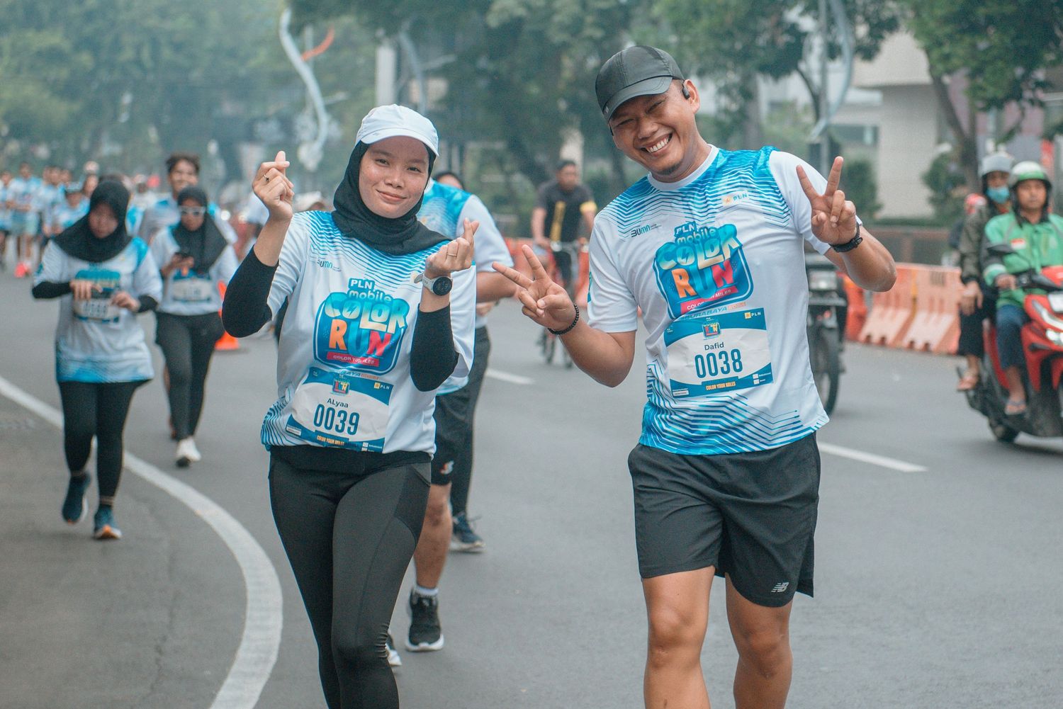 Marathon runners in light blue shirts participate in a group race event on a city street.