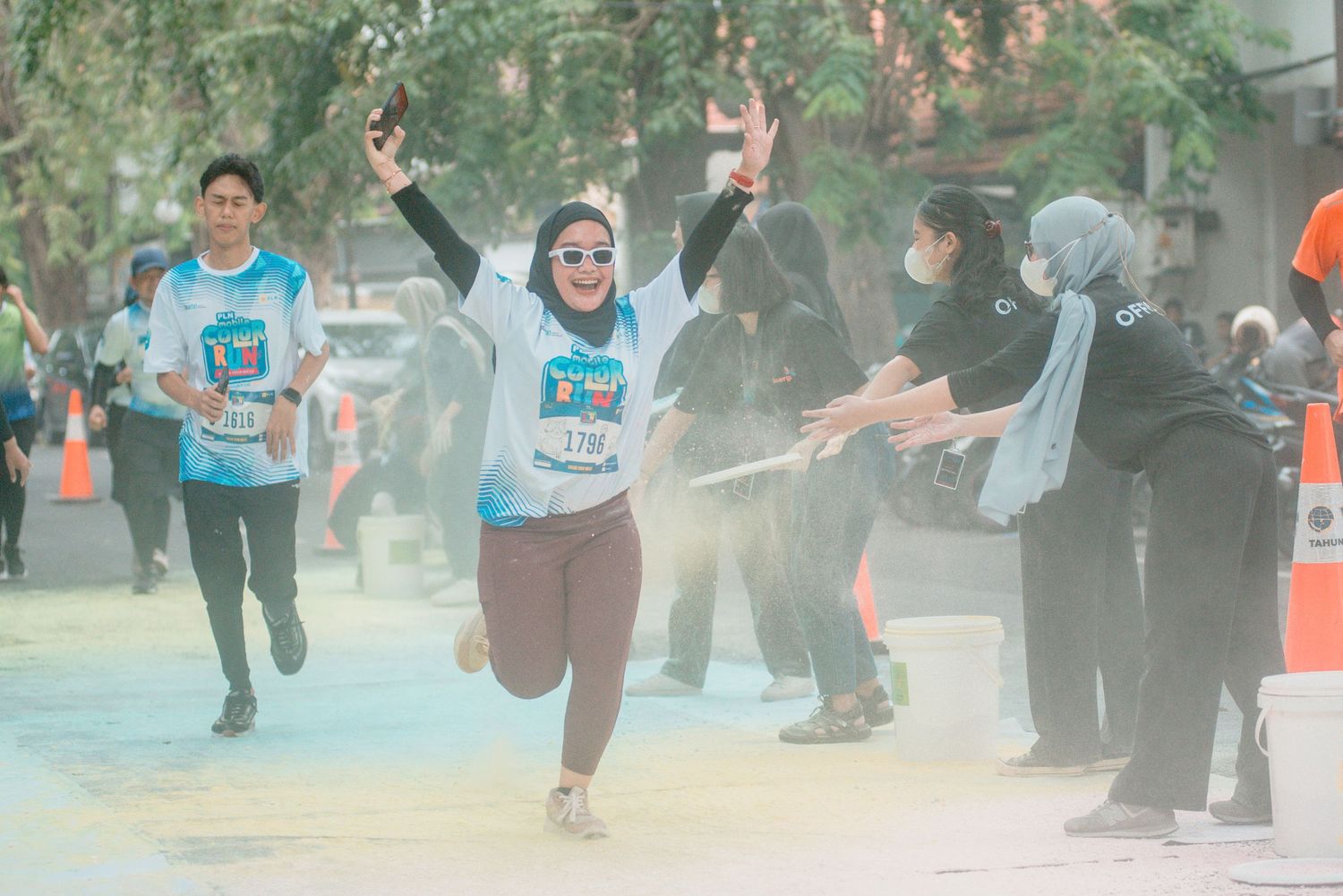 Participants run through a colorful race course while spectators cheer them on during an outdoor event.