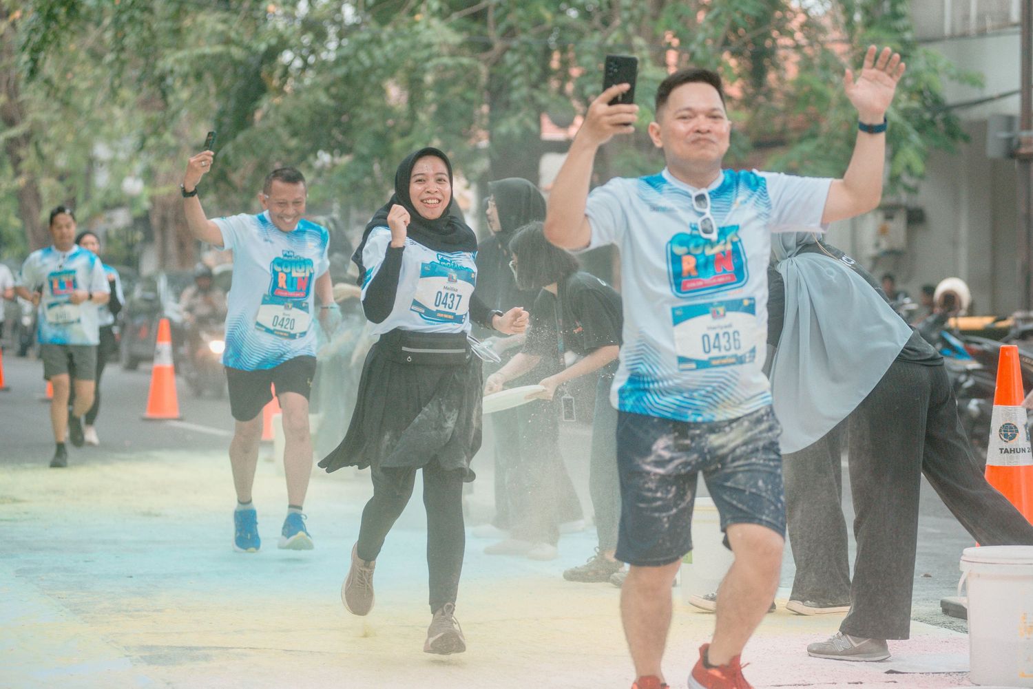 Marathon runners participate in a city race wearing blue race bibs and athletic gear on an urban street course.