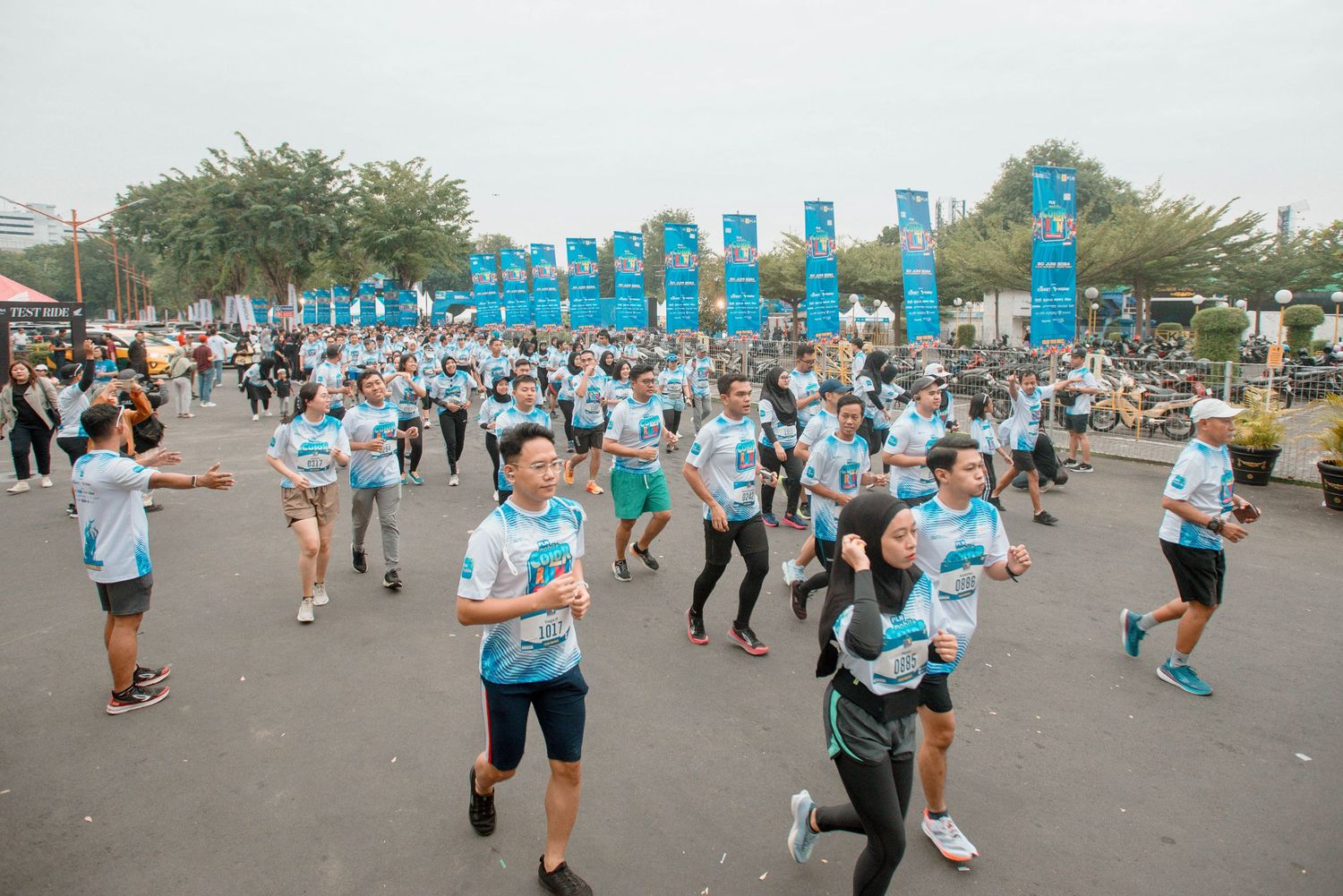 Crowd of participants in light blue shirts running through a street with tall blue banners at an outdoor event.
