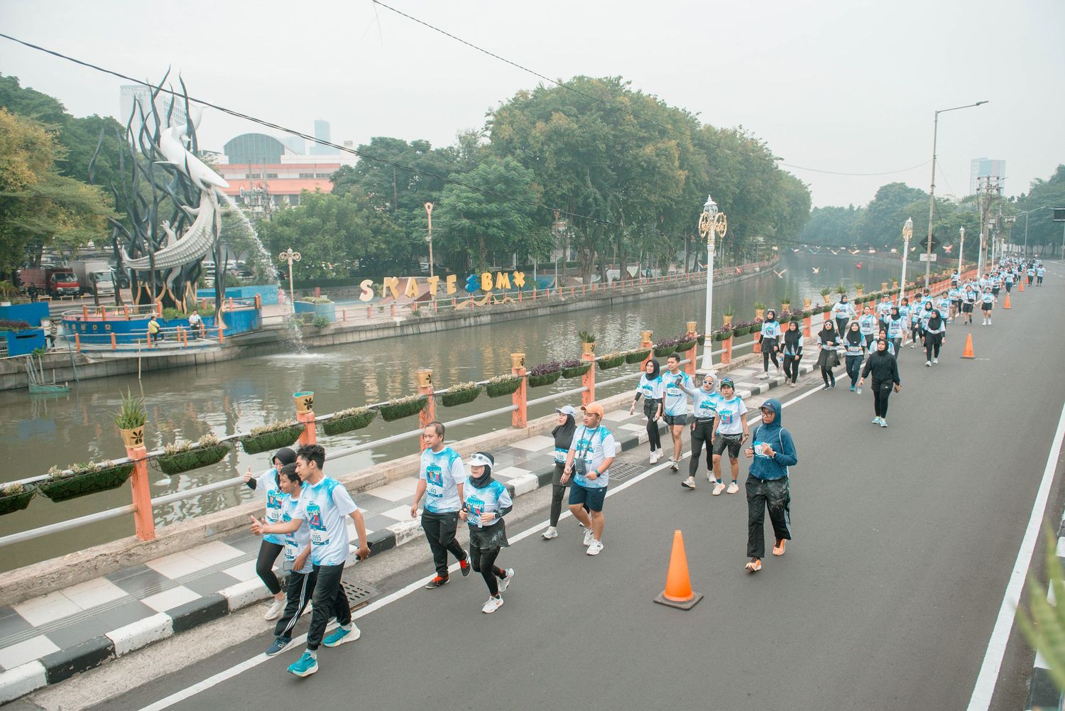 Runners spread across a wide city street during a marathon event with trees lining the roadway.