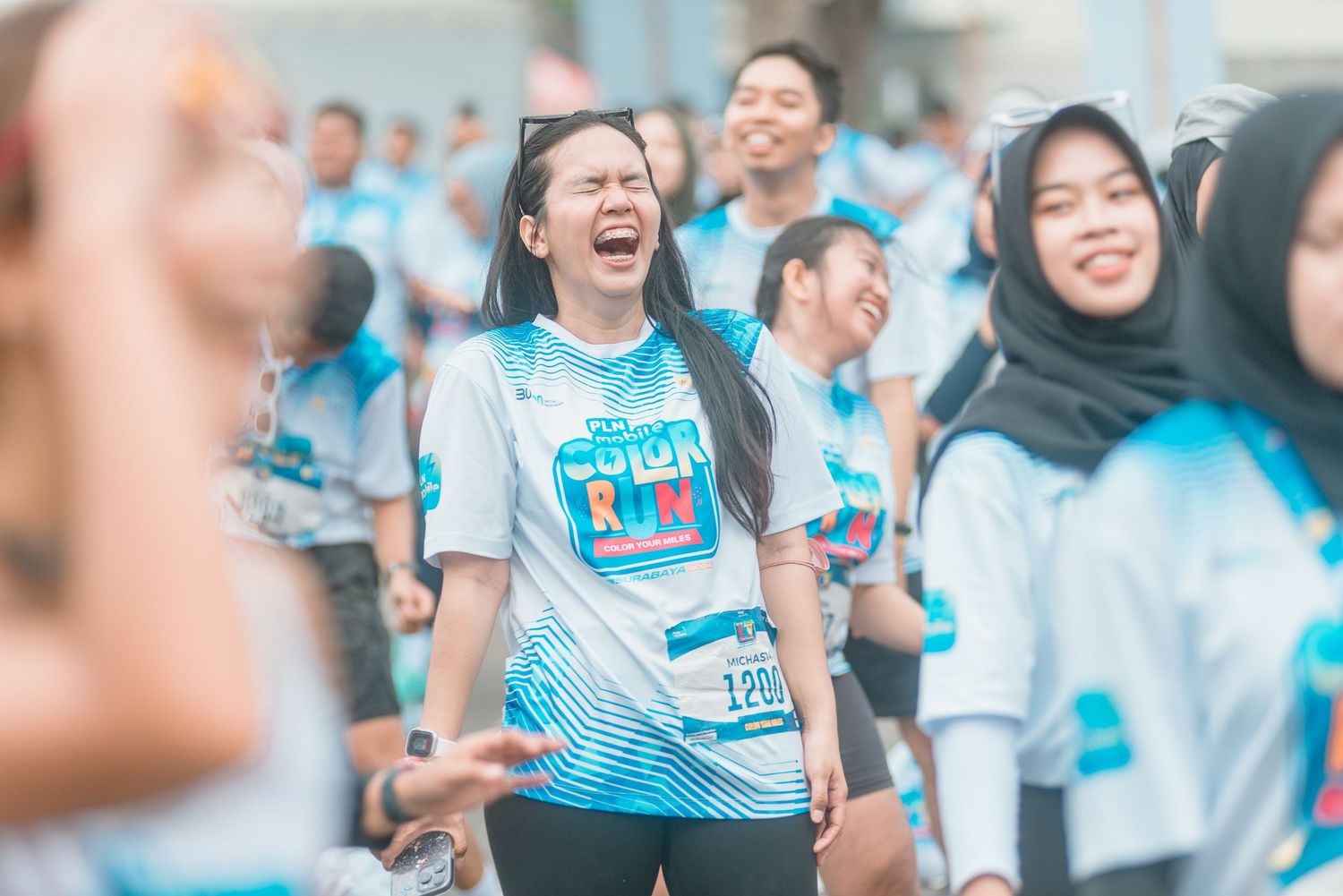 A group of people in light blue shirts laugh together during a cheerful outdoor event.