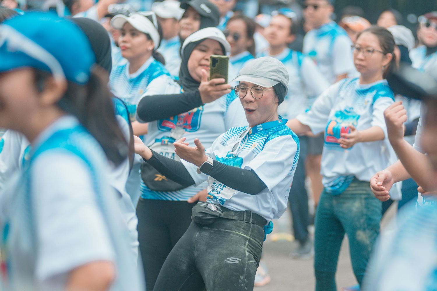 A crowd of people in light blue shirts celebrates by spraying champagne and cheering outdoors.