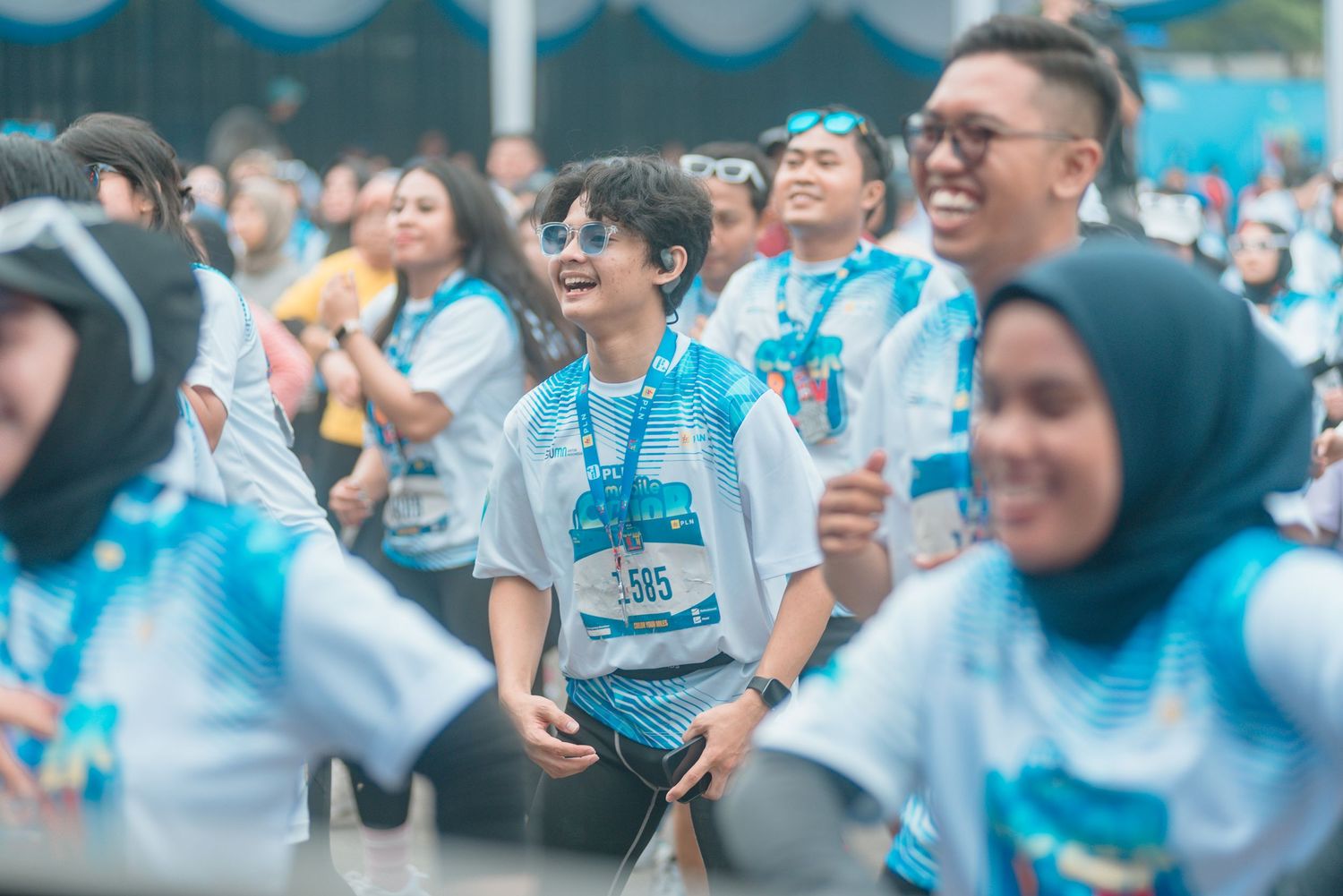 Enthusiastic crowd in light blue and white shirts cheering and celebrating during a daytime gathering.