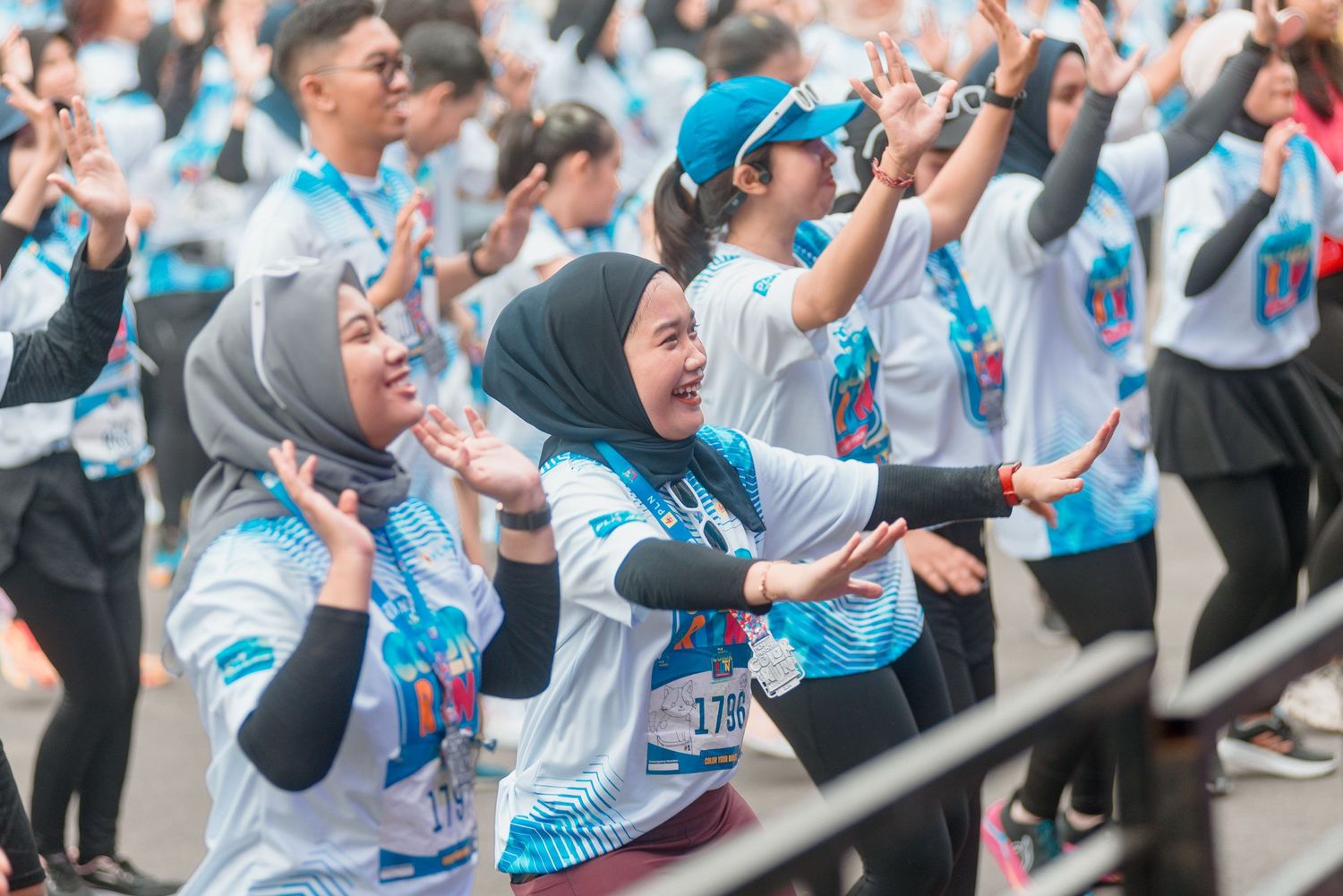 Marathon runners in light blue shirts raise their arms in celebration during a race event.