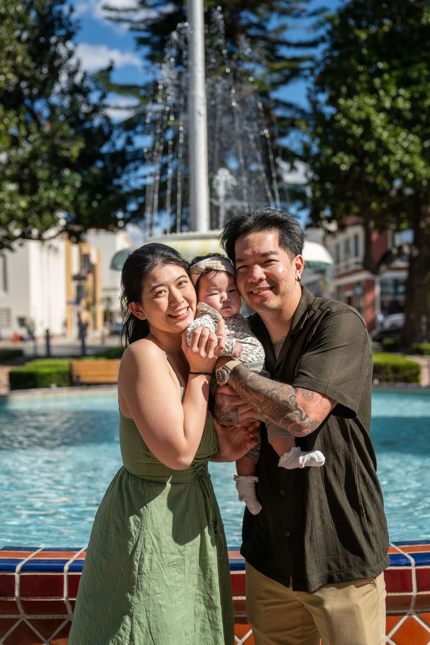 A couple shares a playful moment together on a sunny day by the water with trees in the background.