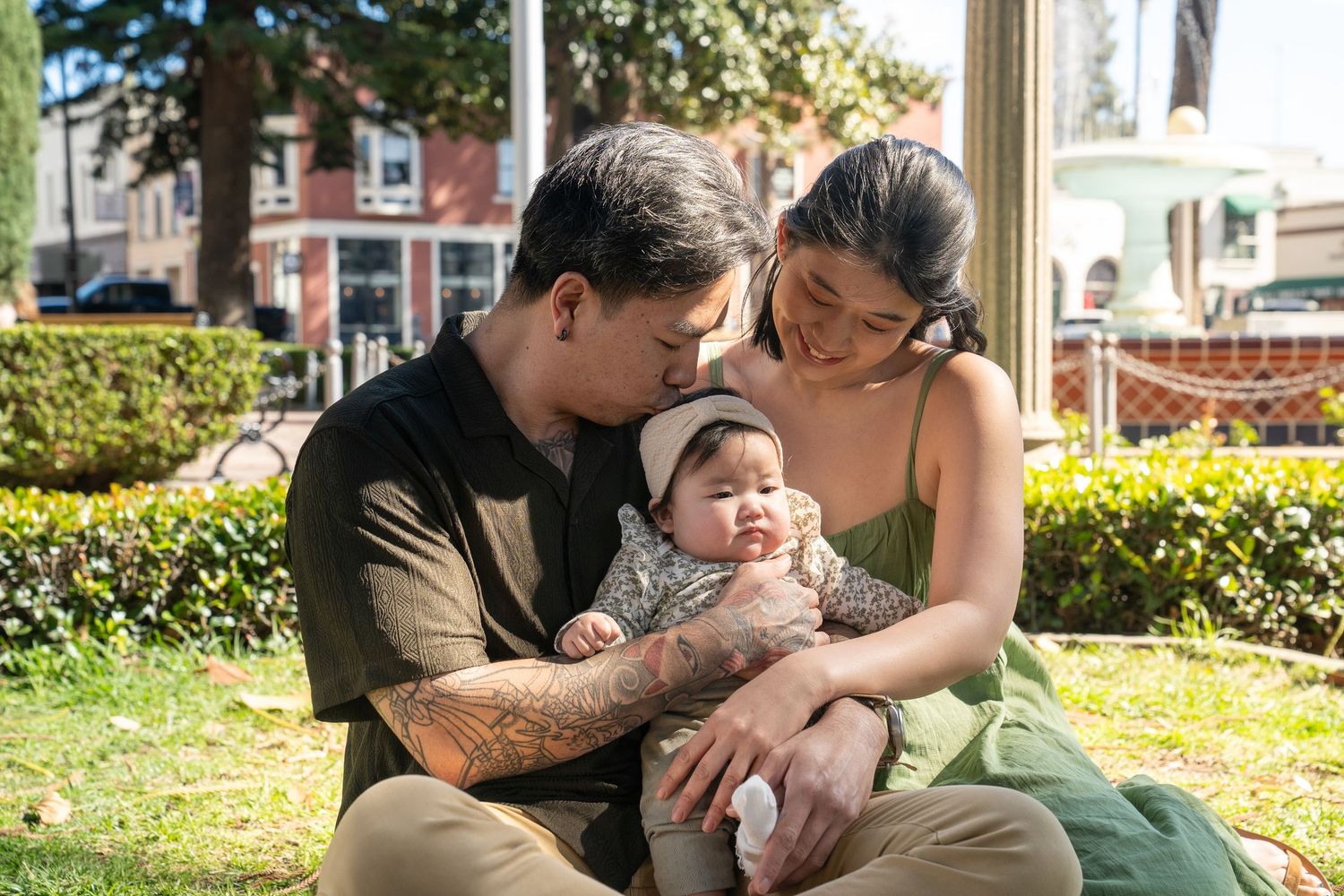 A loving family shares tender moments together while relaxing outdoors in a park setting on a sunny day.