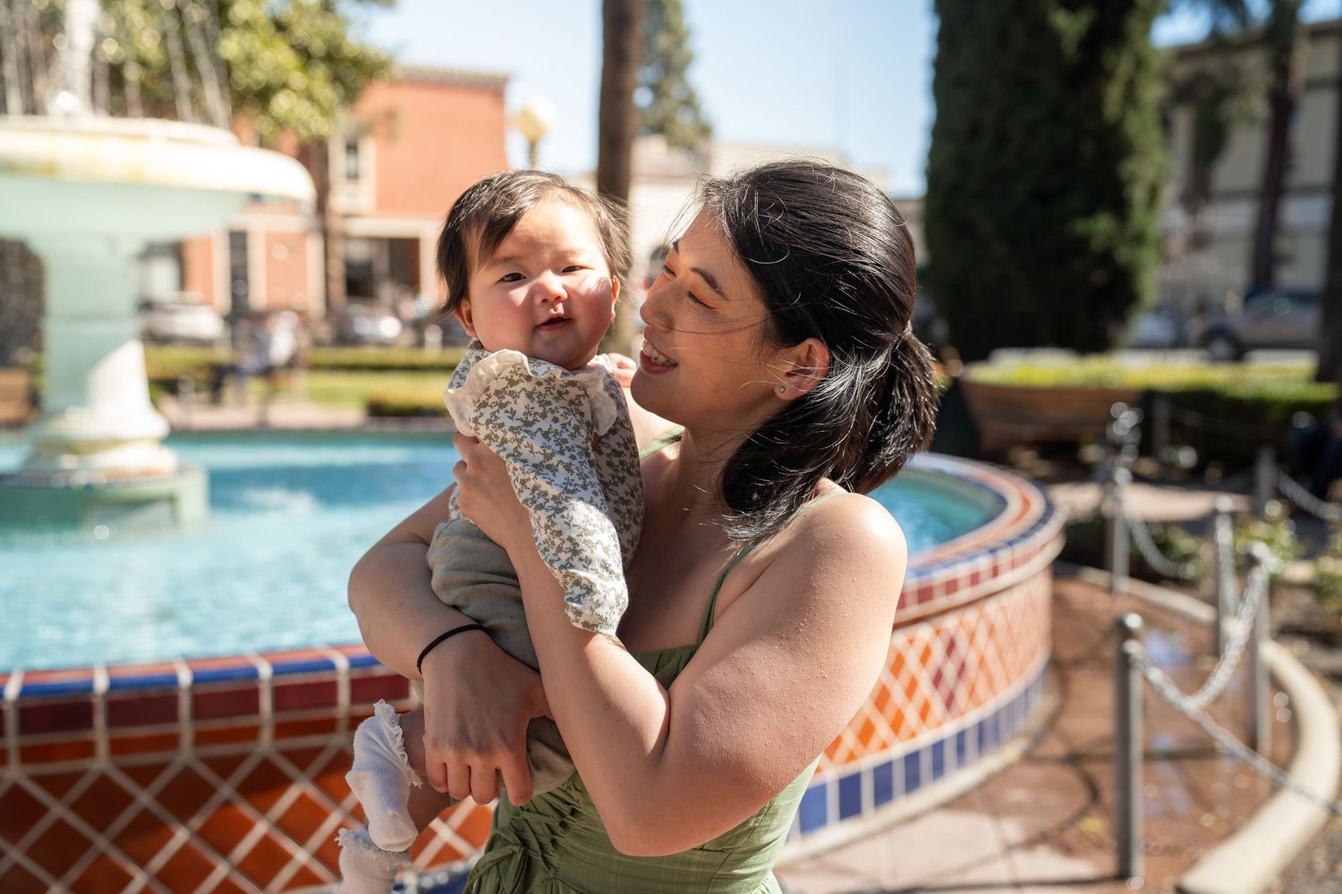 Parent and child share a tender moment while playing in a swimming pool on a sunny day.