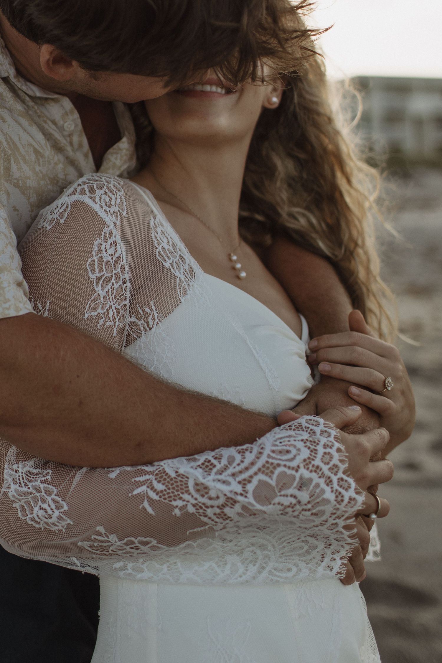A romantic couple embraces on a sandy beach at sunset with the ocean in the background.