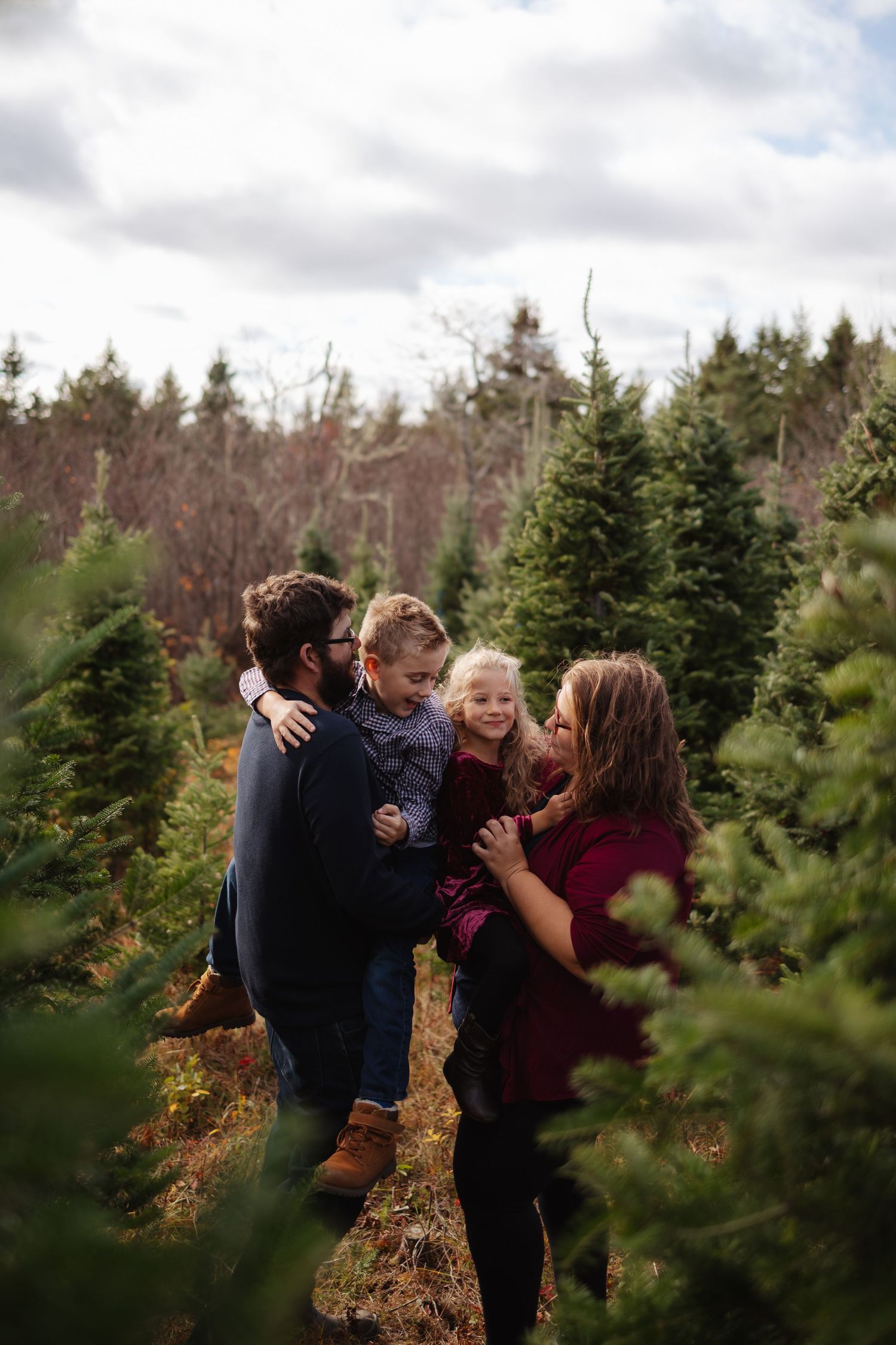 Thalie photography Happy family with two young children enjoying a Christmas tree farm outing together.