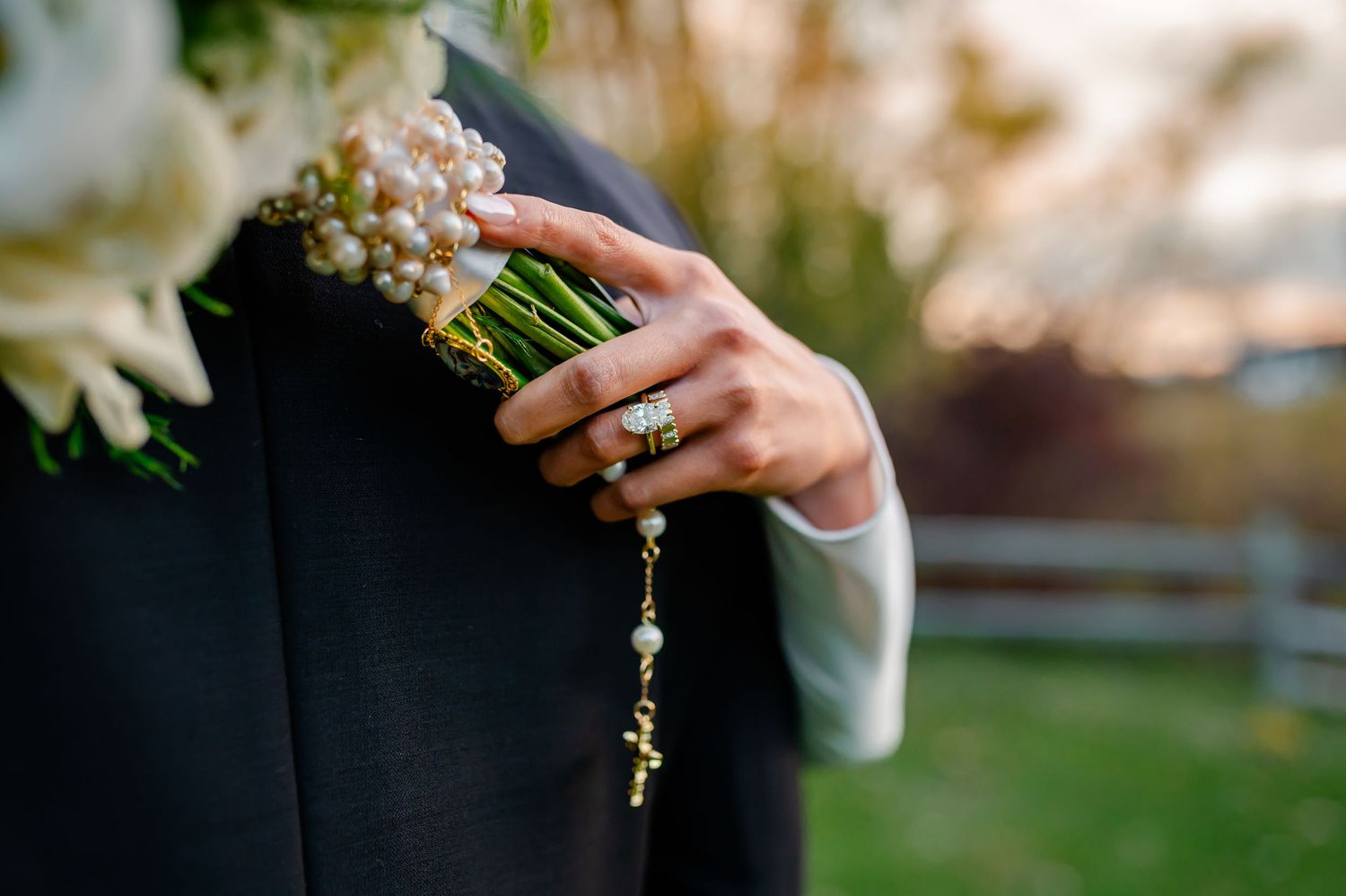 A close-up detail of a wedding bouquet being held against a black formal suit.