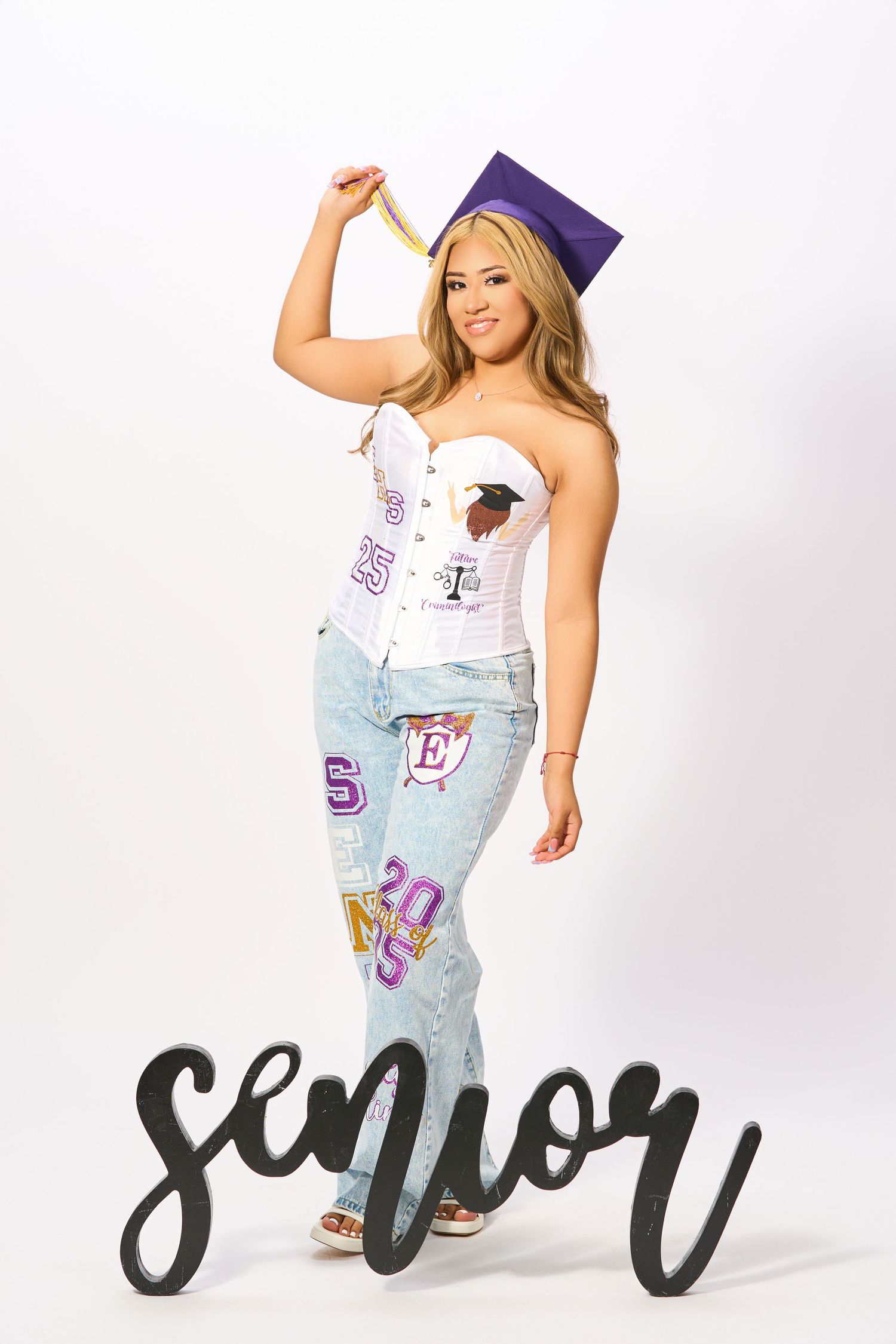 Graduate in purple cap poses in white corset top and decorated denim jeans with 'Senior' text overlay.