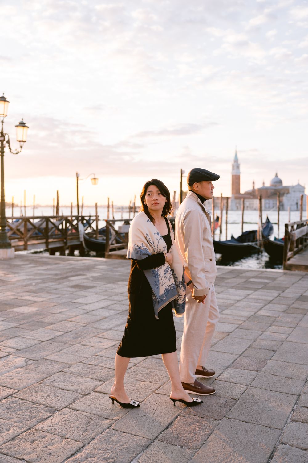 Stone walkway along Venice's waterfront with traditional lampposts and gondolas at dusk.