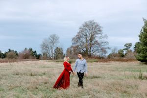 Two people in flowing red and blue capes walk through a misty autumn field during a dreamy outdoor photoshoot.