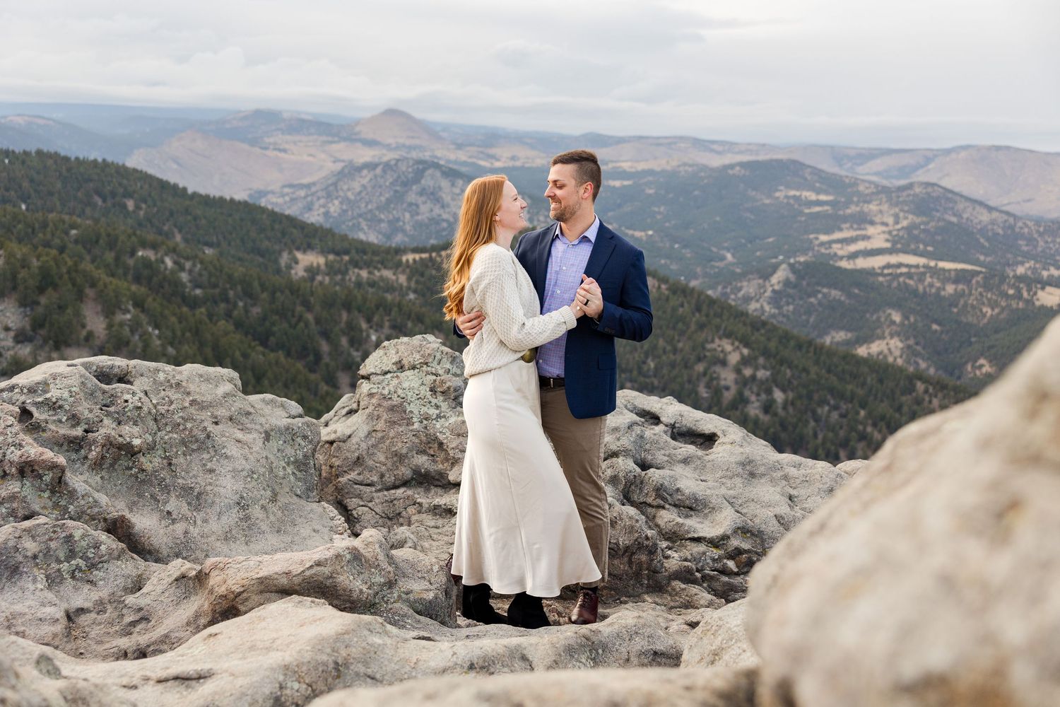A couple in wedding attire shares an intimate moment on a mountain overlook with sweeping valley views in the background.