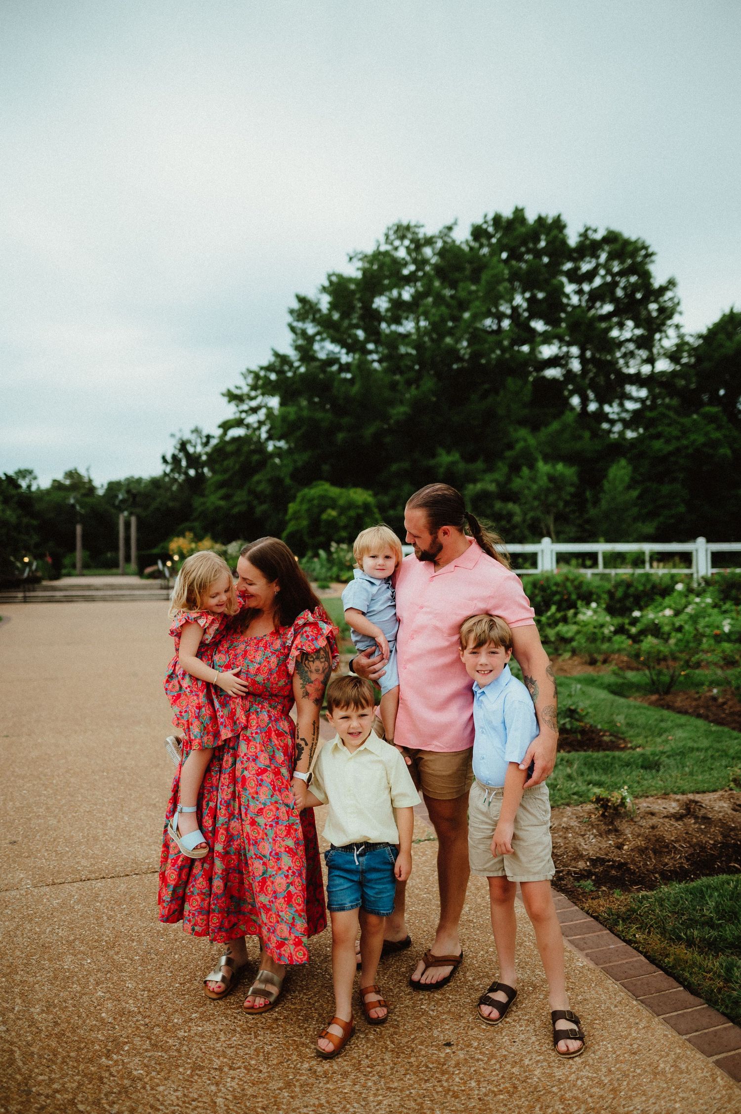 A group walks together on a gravel path through a lush garden setting on a cloudy summer day.
